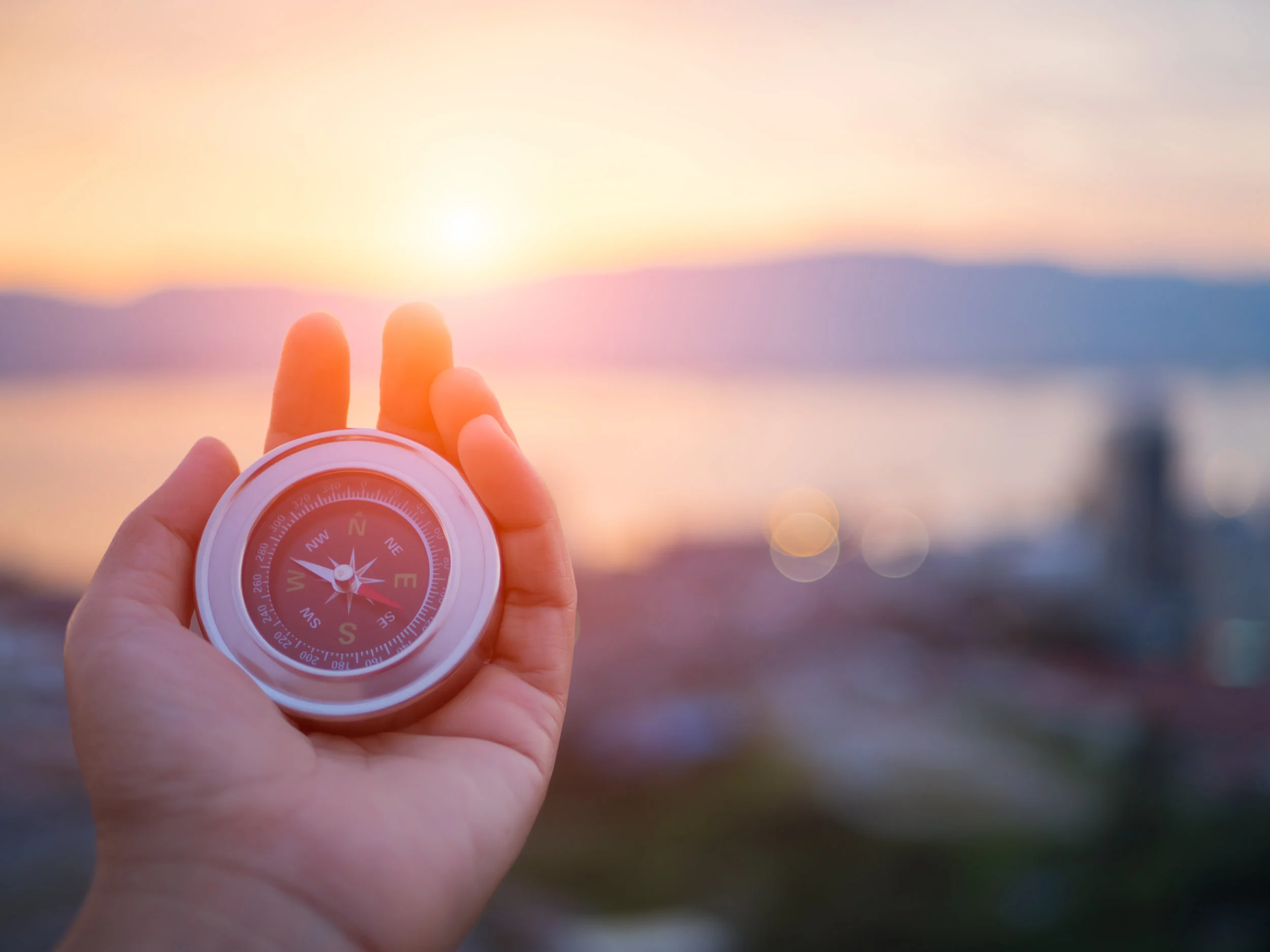 Closeup-hand-holding-compass-with--mountain-and-sunset-sky-background.-838489612_4608x3456.jpeg