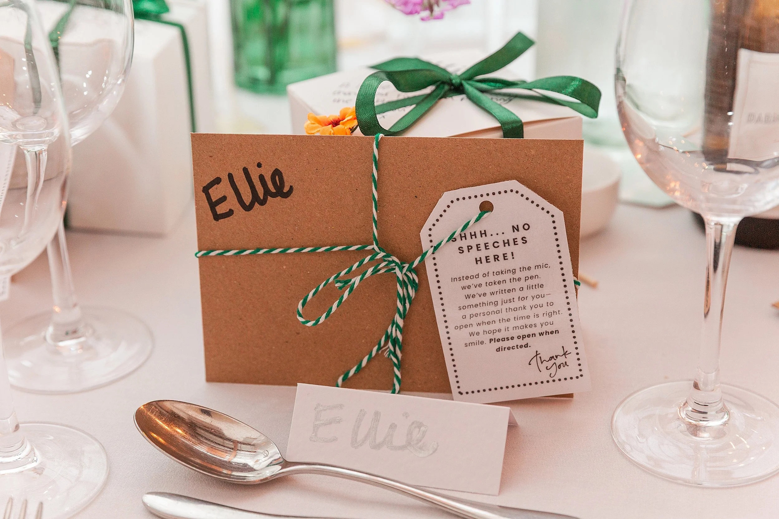 A brown envelope with green and white striped string sitting on a wedding breakfast table with a tag saying "Shh...no speeches here"