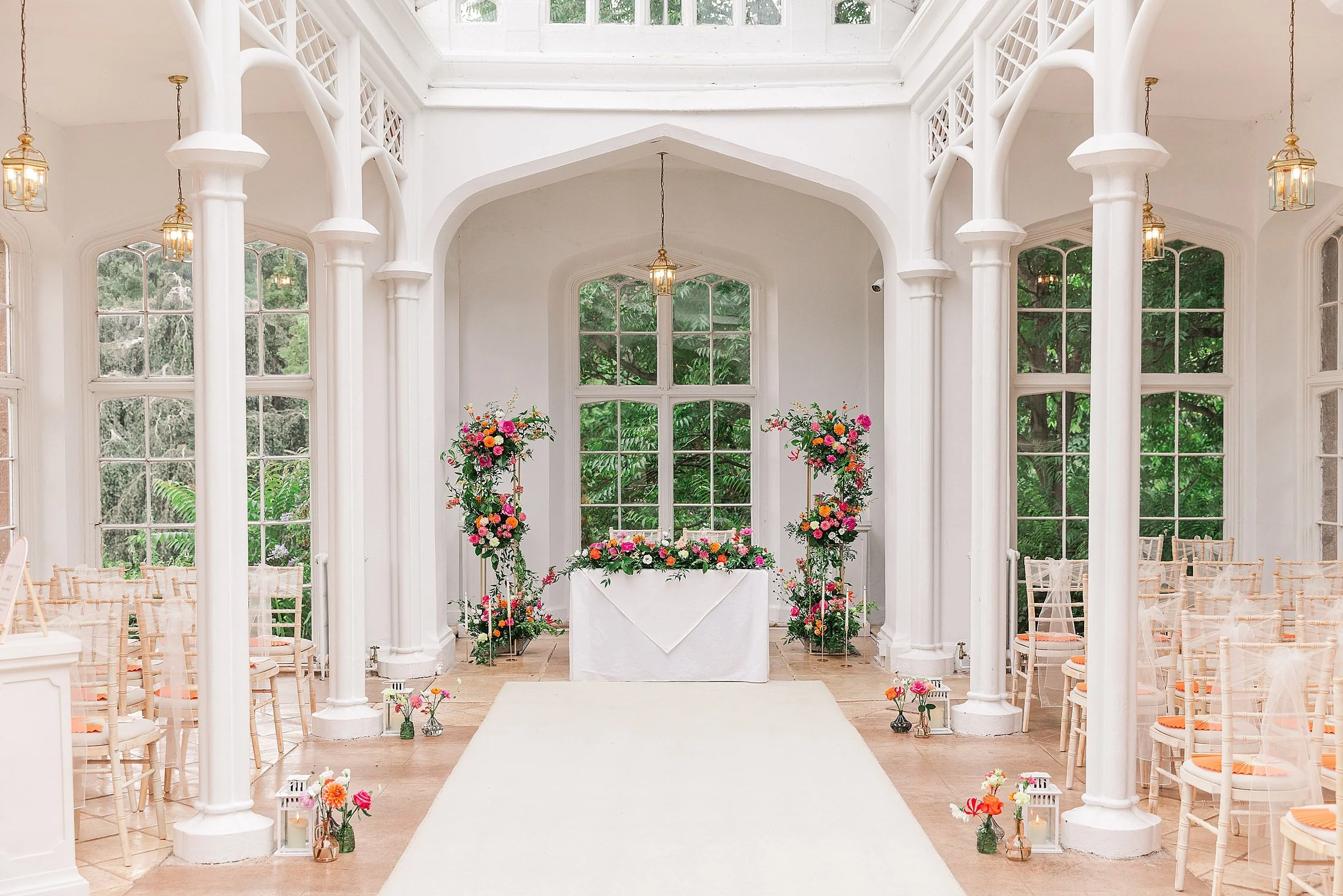 A victorian orangery dressed for a wedding full of colourful flowers of hot pink and bright oranges