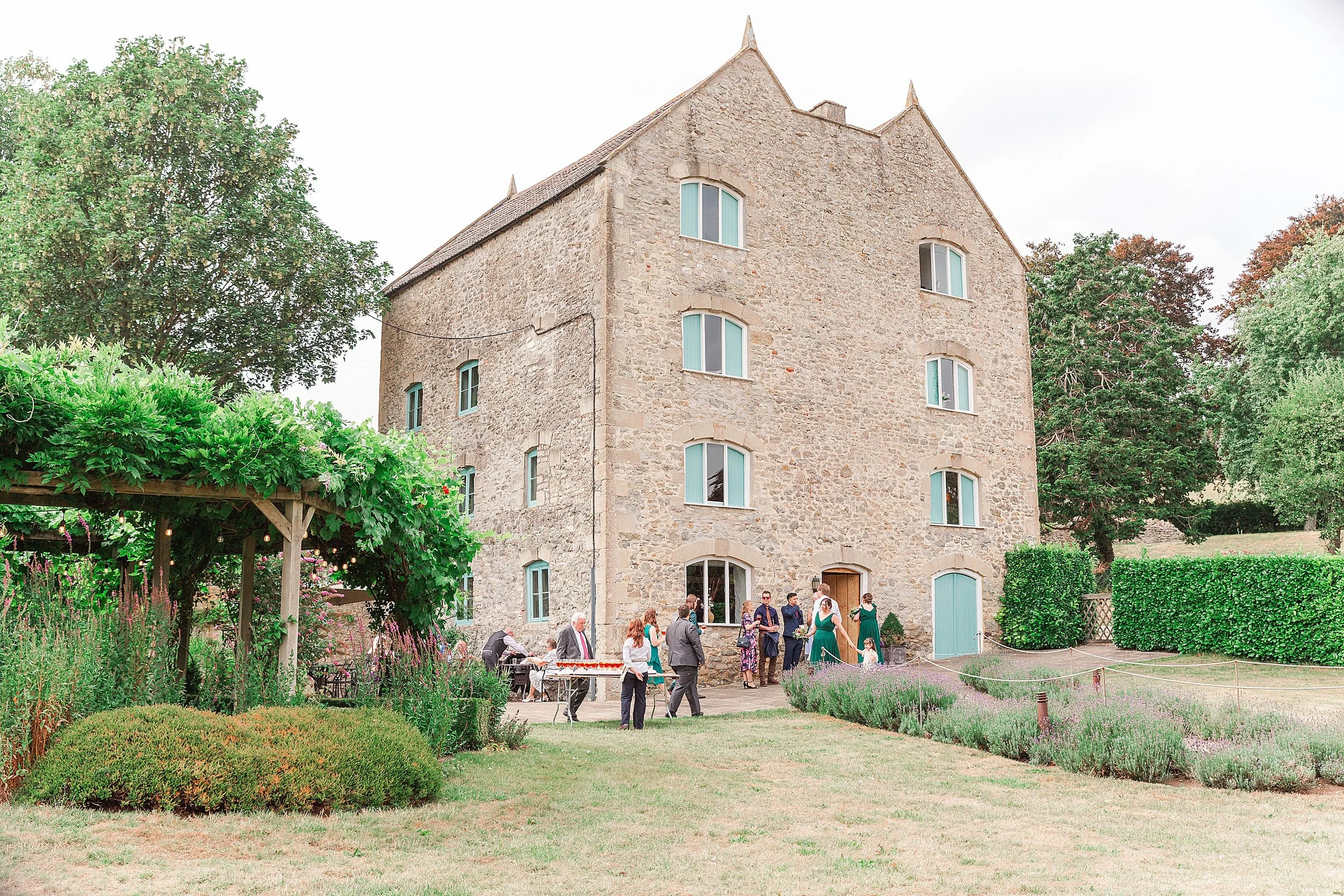 A stone bricked wedding venue with wedding guests mingling in the gardens