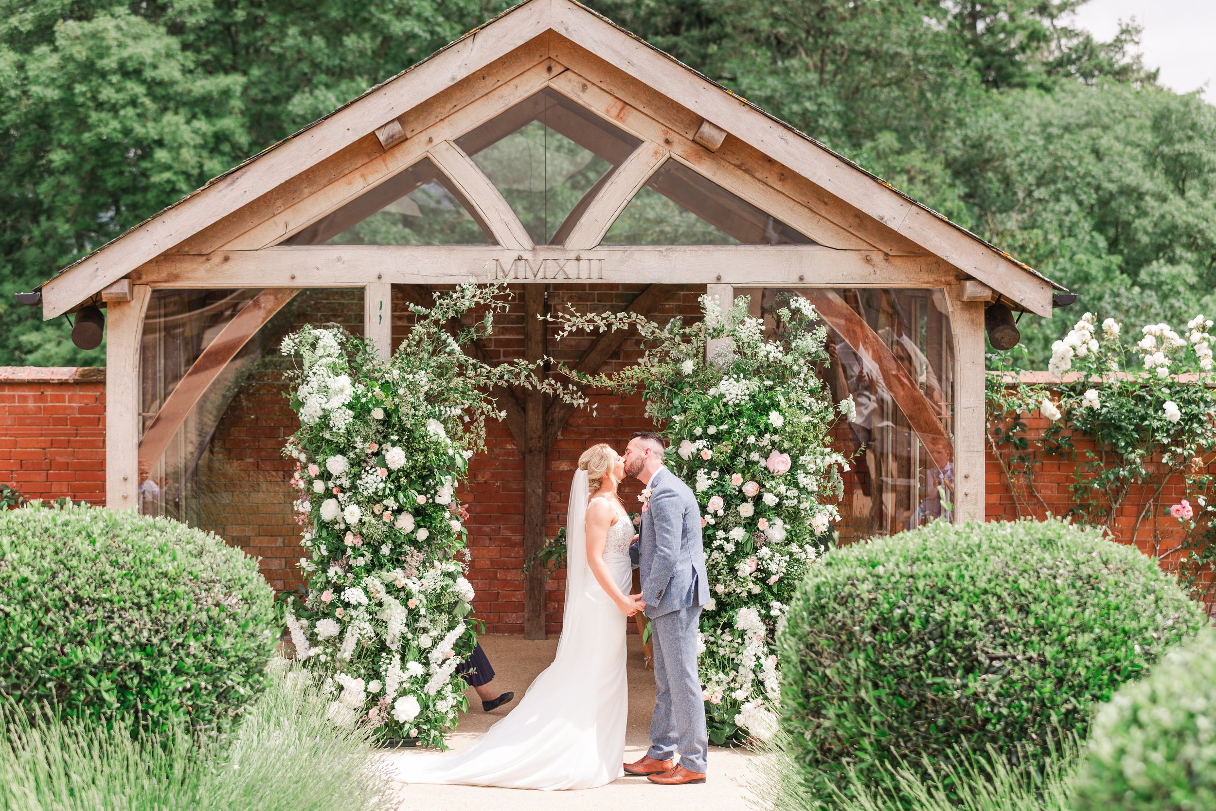 A bride and groom sharing their first kiss in front of a floral arch full of pastel flowers