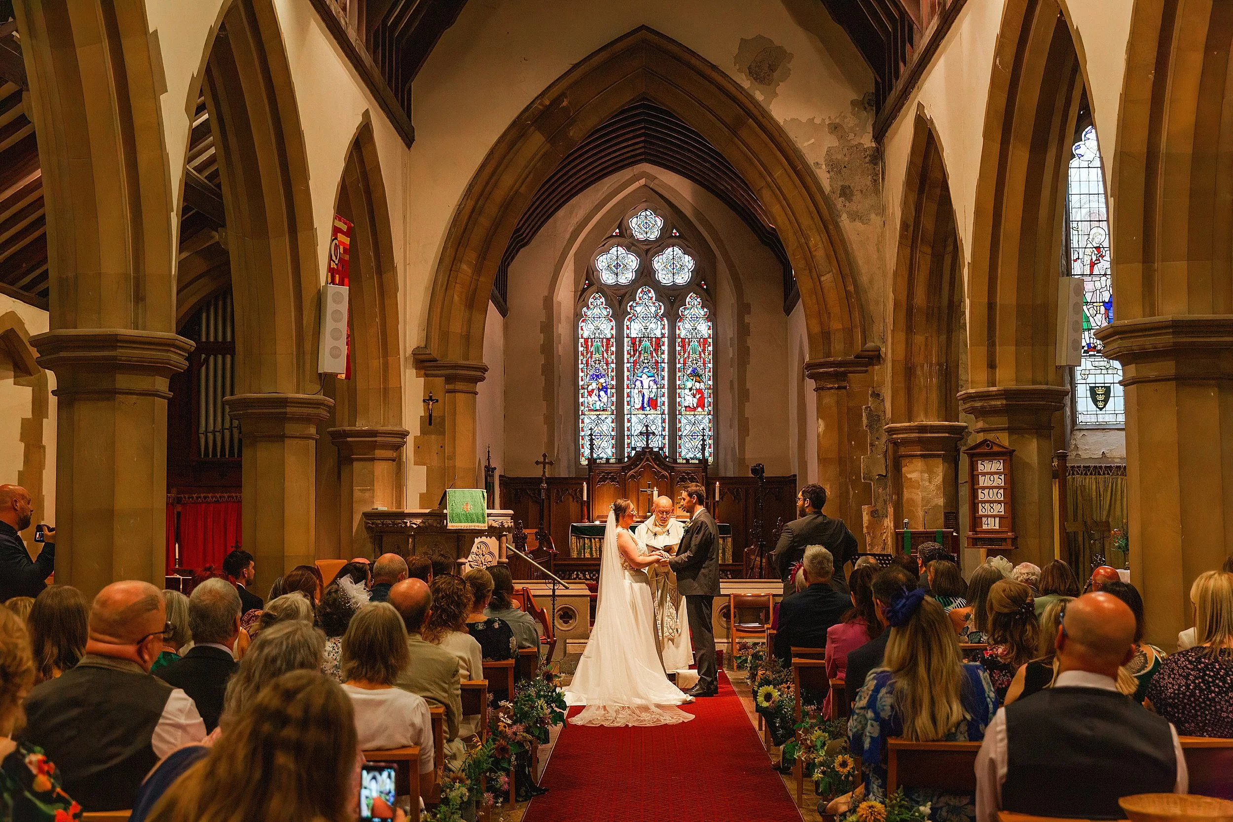 A bride with brown hair and glasses standing at the church alter with her groom in a grey suit