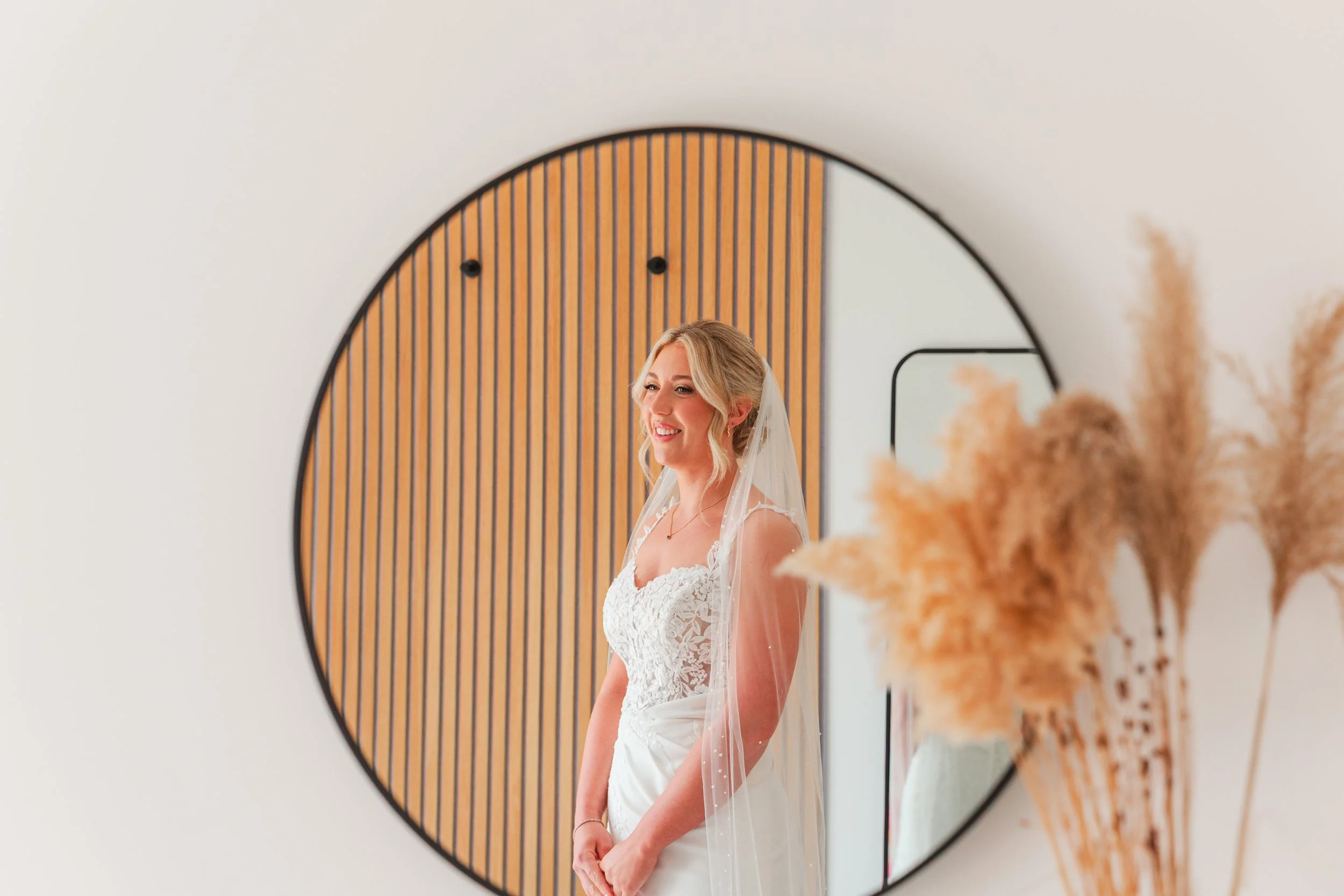 A reflection shot in a round mirror of a bride in a lace dress and veil