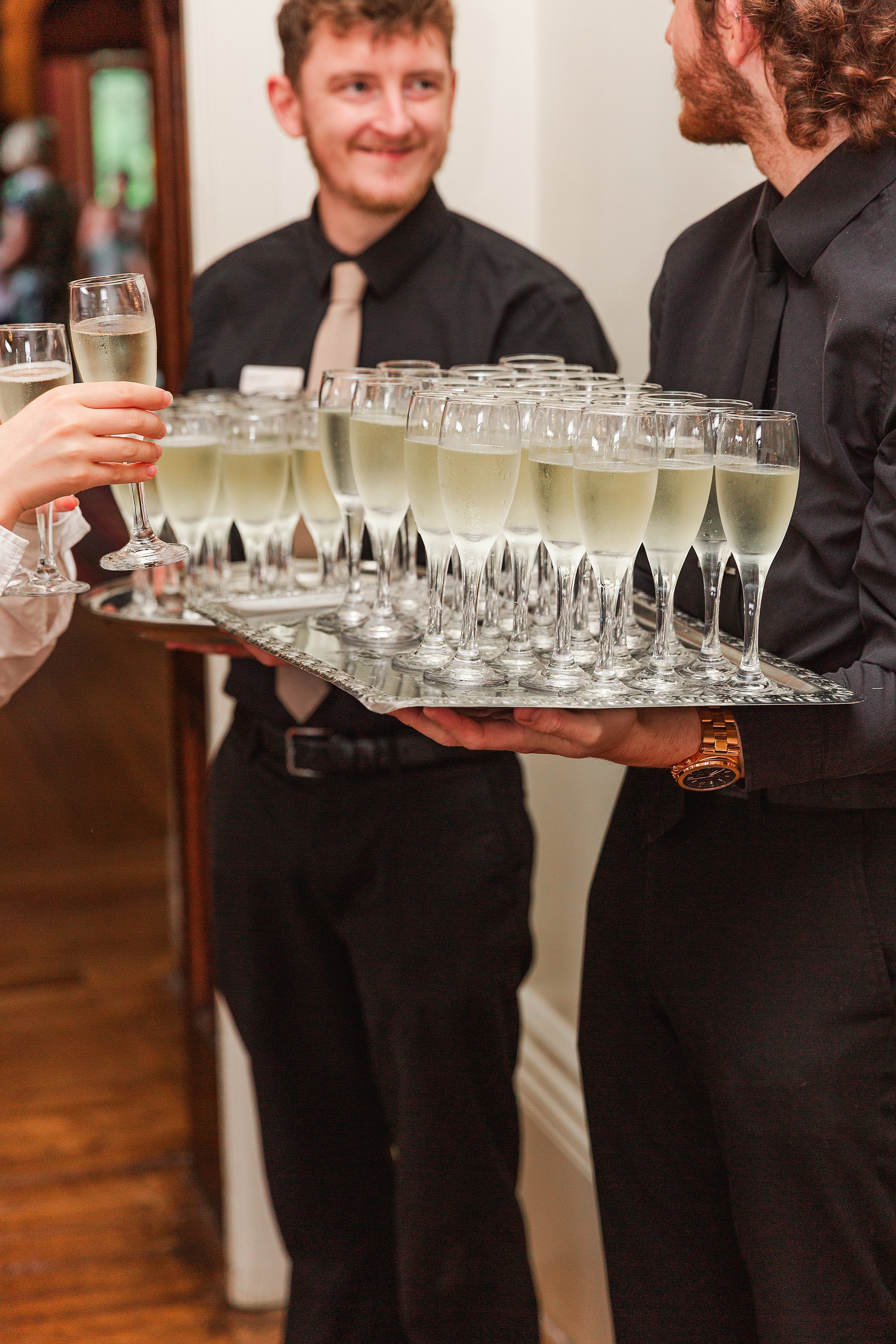 A barman dressed in black holding a tray of champagne flutes