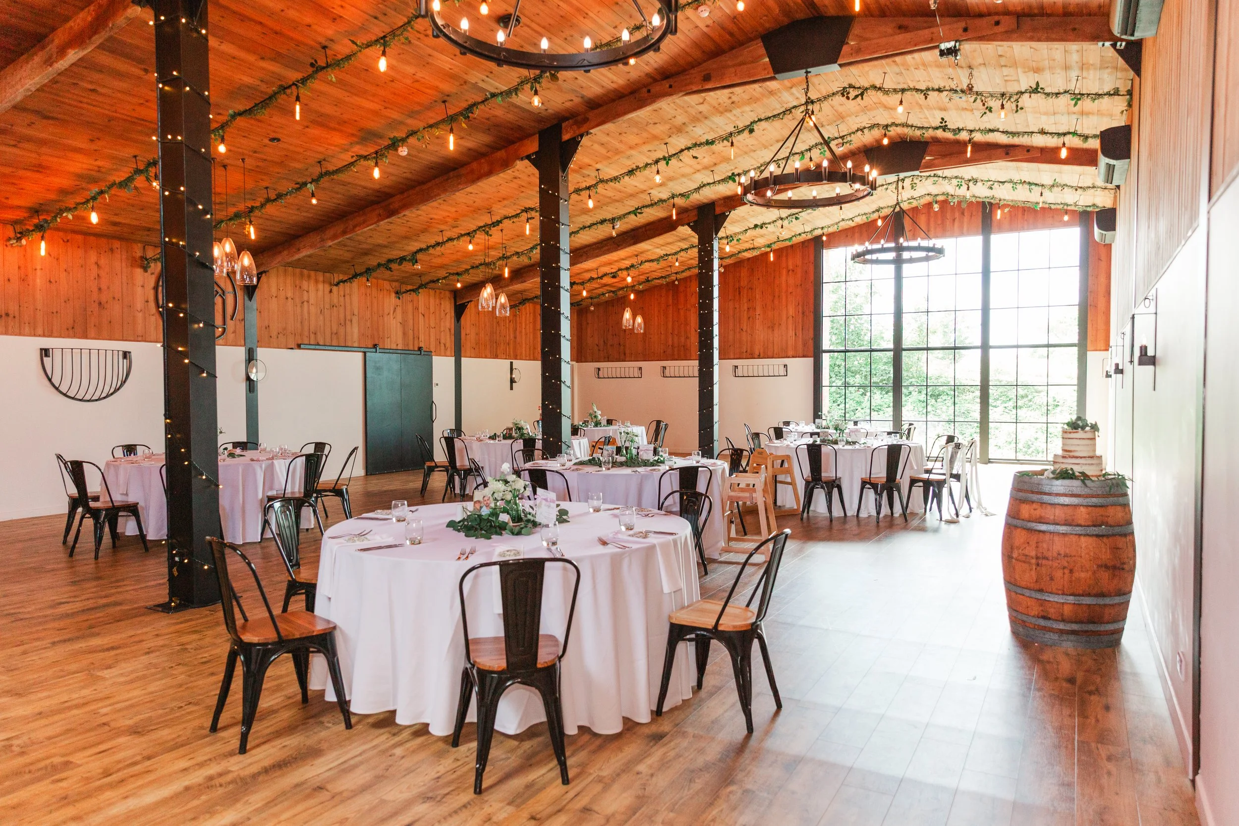 A wedding breakfast room at a barn venue in Devon with wooden beams and black chandeliers with candlelights on the ceiling