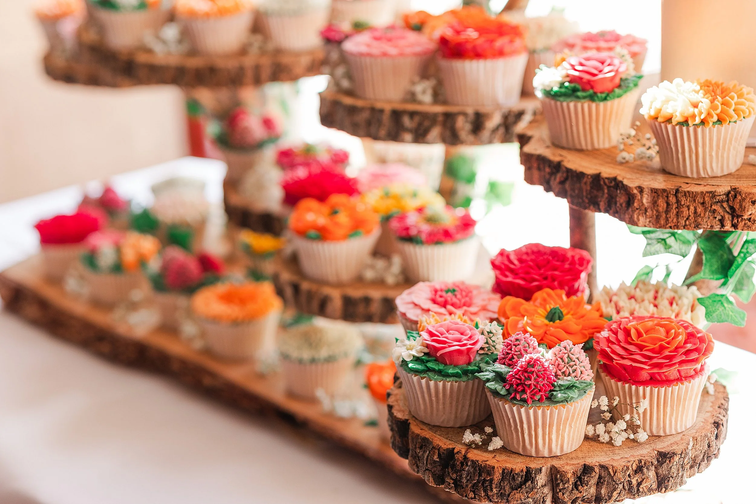 A photo full of pretty colourful floral cupcakes on wood slices