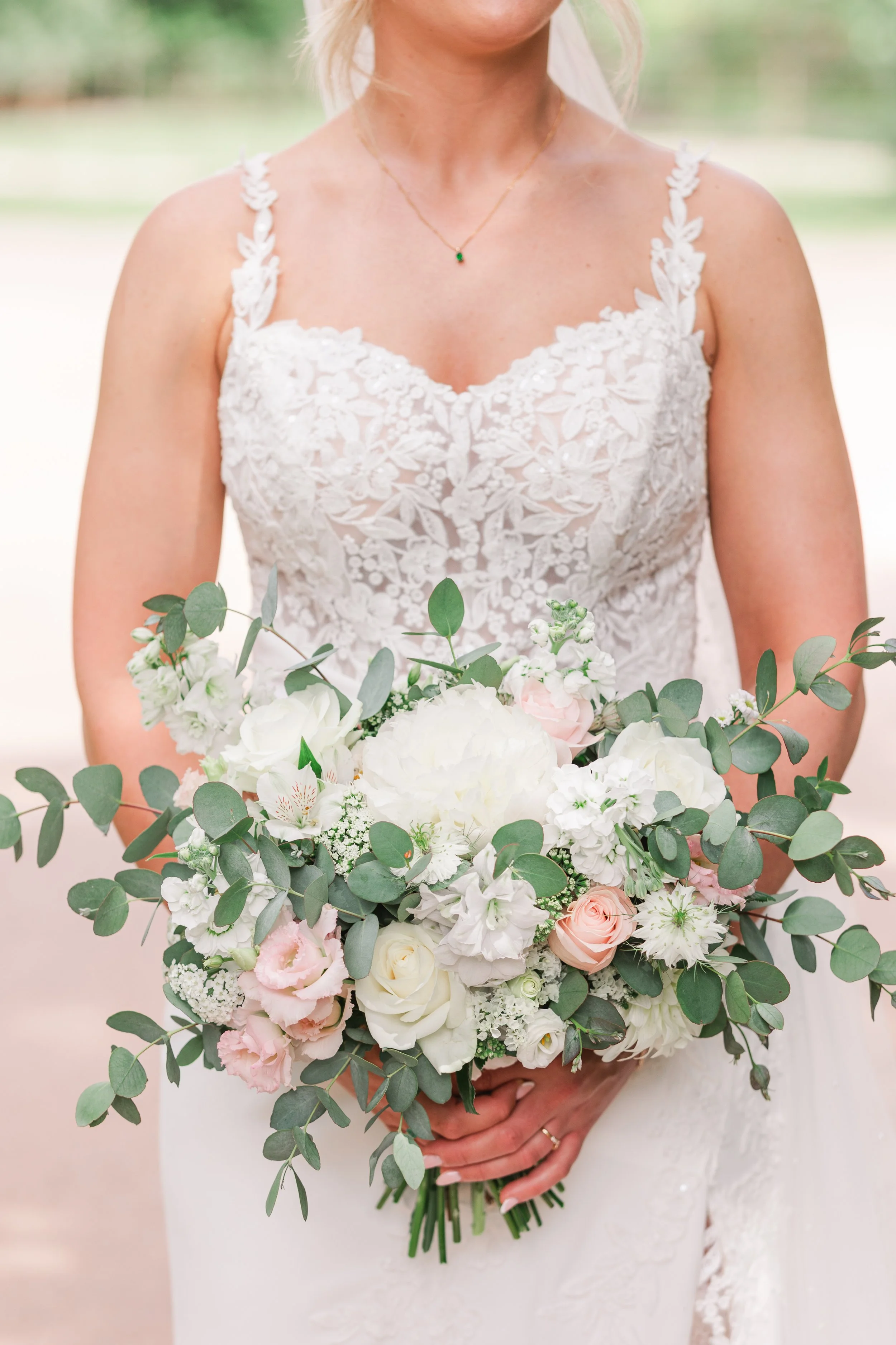 A close up of a bride in a lace dress holding a pretty pastel wedding boquet