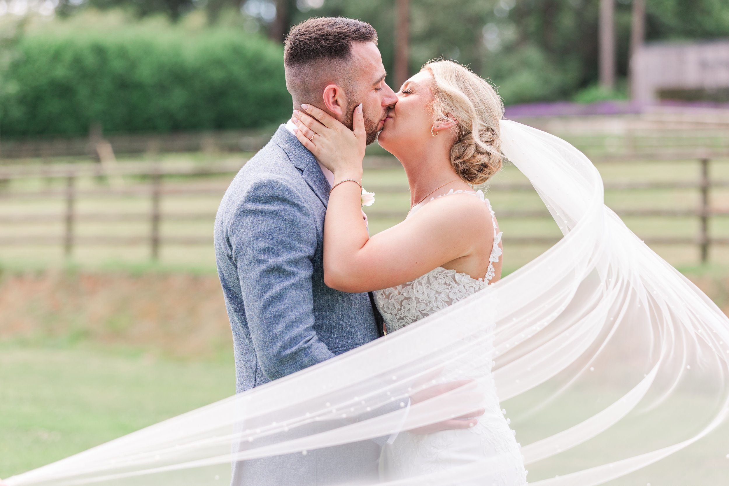 A bride with her veil flying kissing her groom dressed in a blue suit