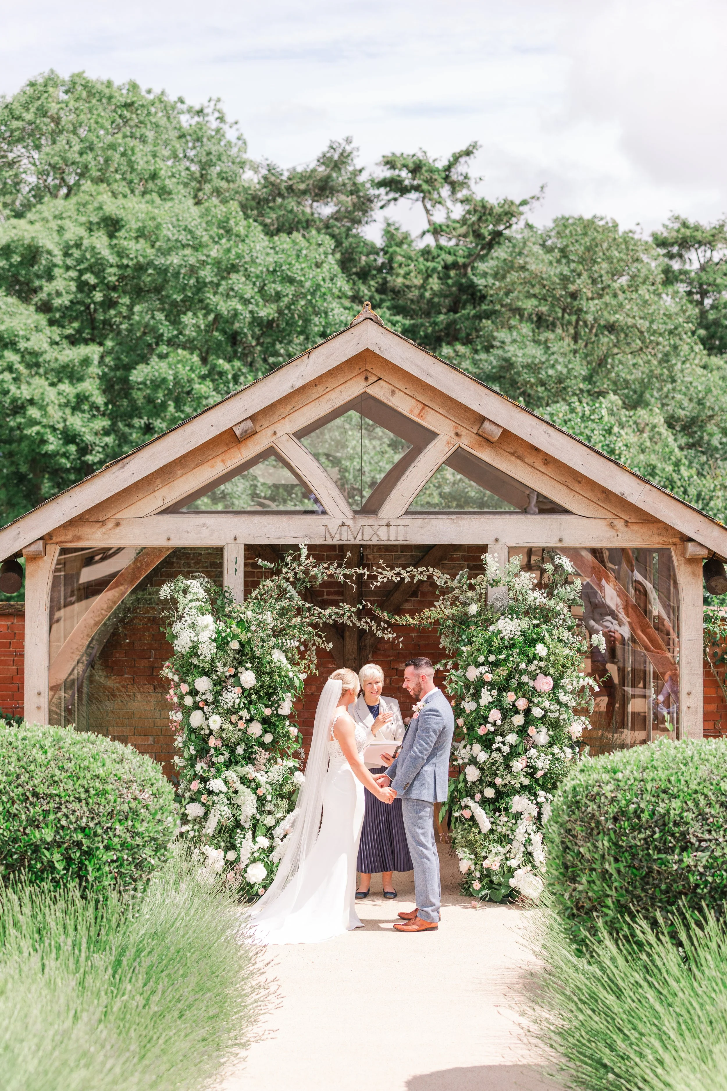 A bride and groom at an outdoor ceremony in a walled garden in Devon surrounded by Florals
