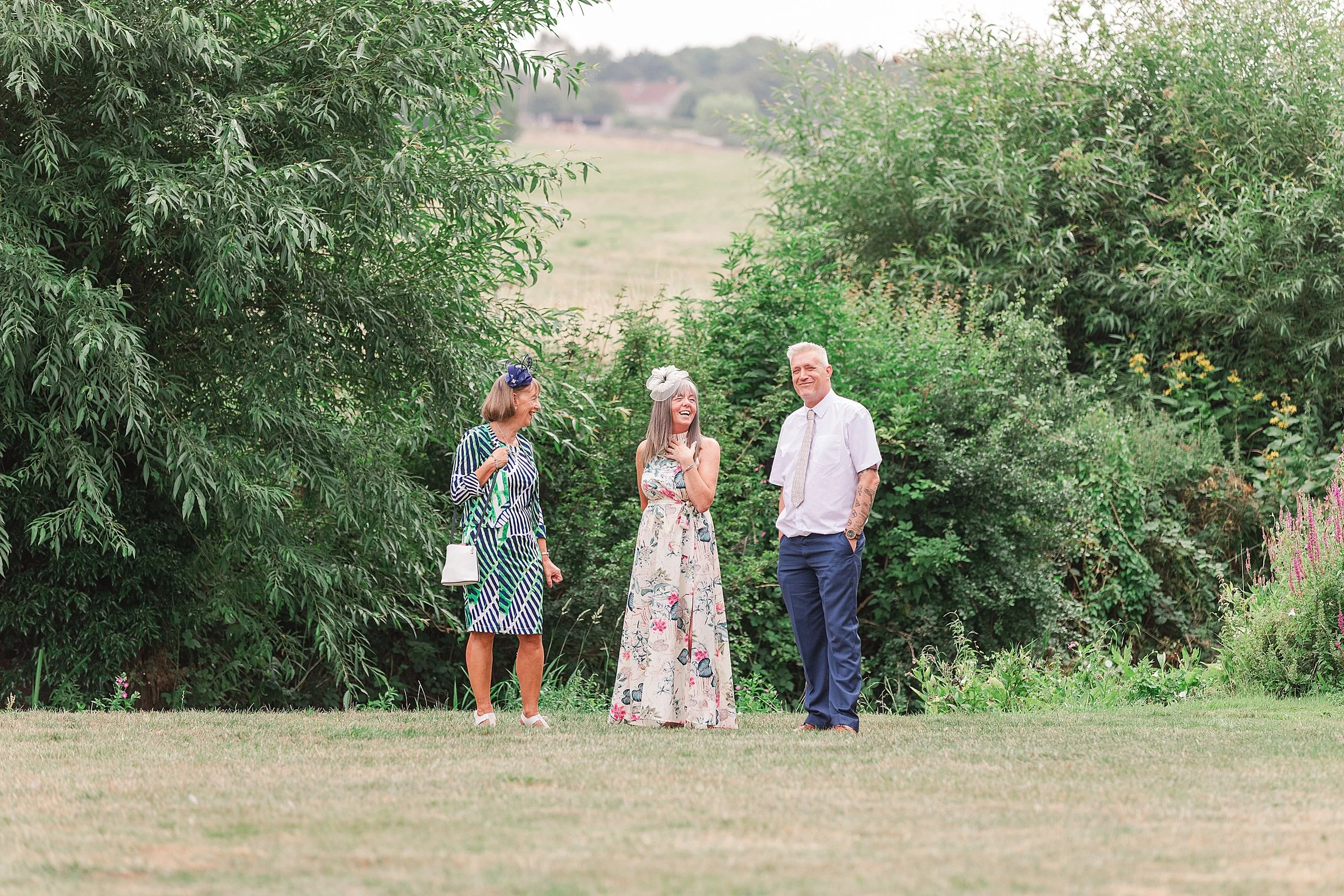 3 wedding guests standing in an English country garden enjoying a drink
