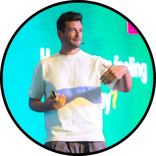 Image of Roy speaking at a conference on stage behind a bright green background