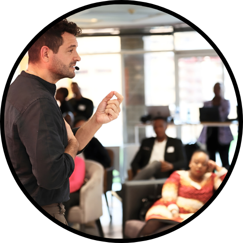 Image of Roy speaking to an audience in a well lit room, looking intense