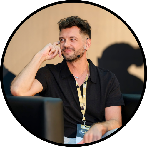 Circular image of Roy Gluckman seated on a chair on stage, looking at the moderator with a soft smile