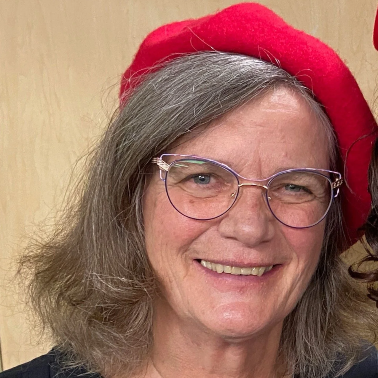 smiling middle-aged white woman with salt and pepper shoulder-length hair, glasses and a red beretblonde hair and glasses
