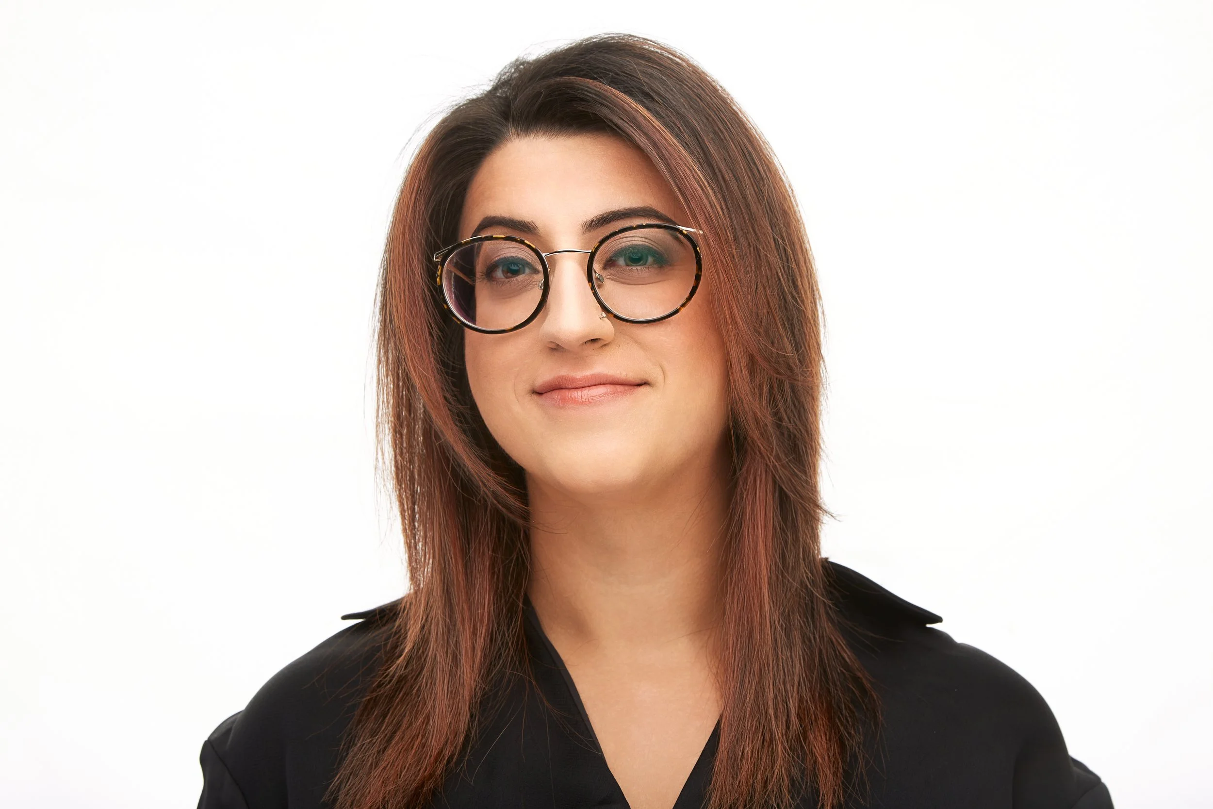 A woman with shoulder-length brown hair, wearing black-rimmed glasses and a black top, smiling against a white background.
