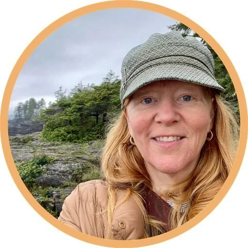 Portland NeuroMovement Practitioner Phoebe MacRae looking deirectly at the camera, on the westcoast rocks, wearing a peaked hat!