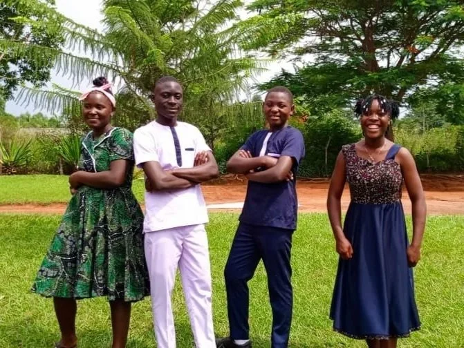 4 confident, happy Ugandan teenagers, standing in a row smiling.
