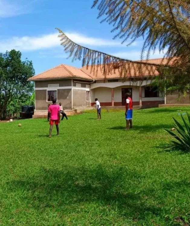 5 children playing football on lush grass, outside a large house with a terracotta-tiled roof.