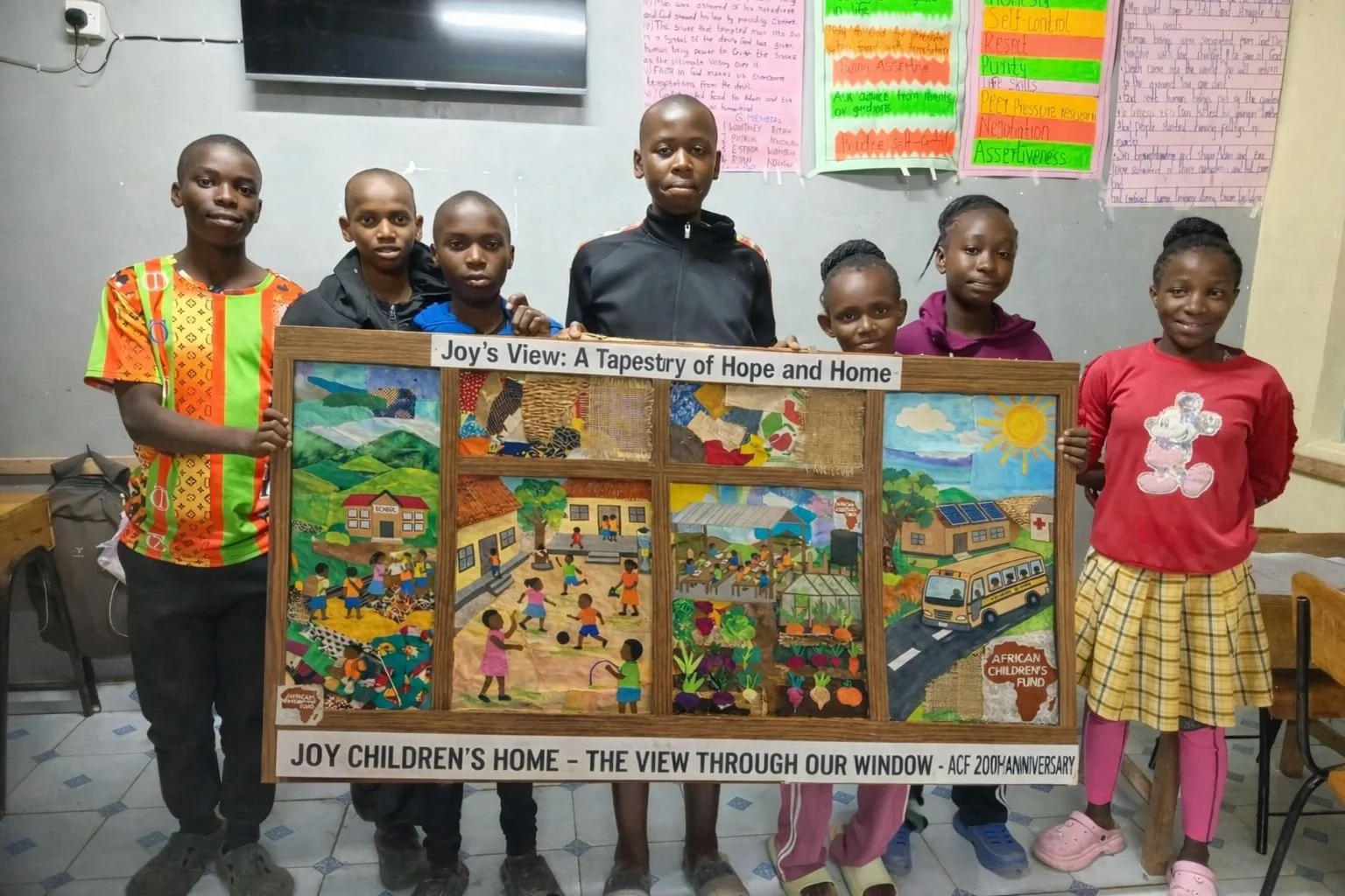 7 smiling Kenyan children, standing beside the tapestry they have helped create. It's headed "Joy's View: A Tapestry of Hope and Home".