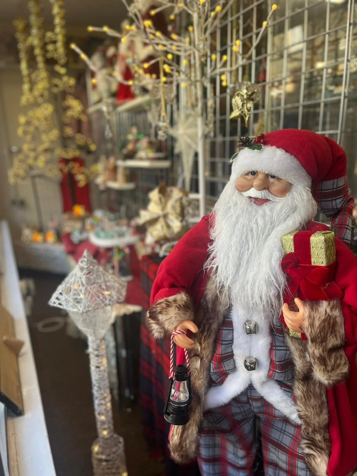A giant Santa Claus figurine in front of a festive charity shop window display.
