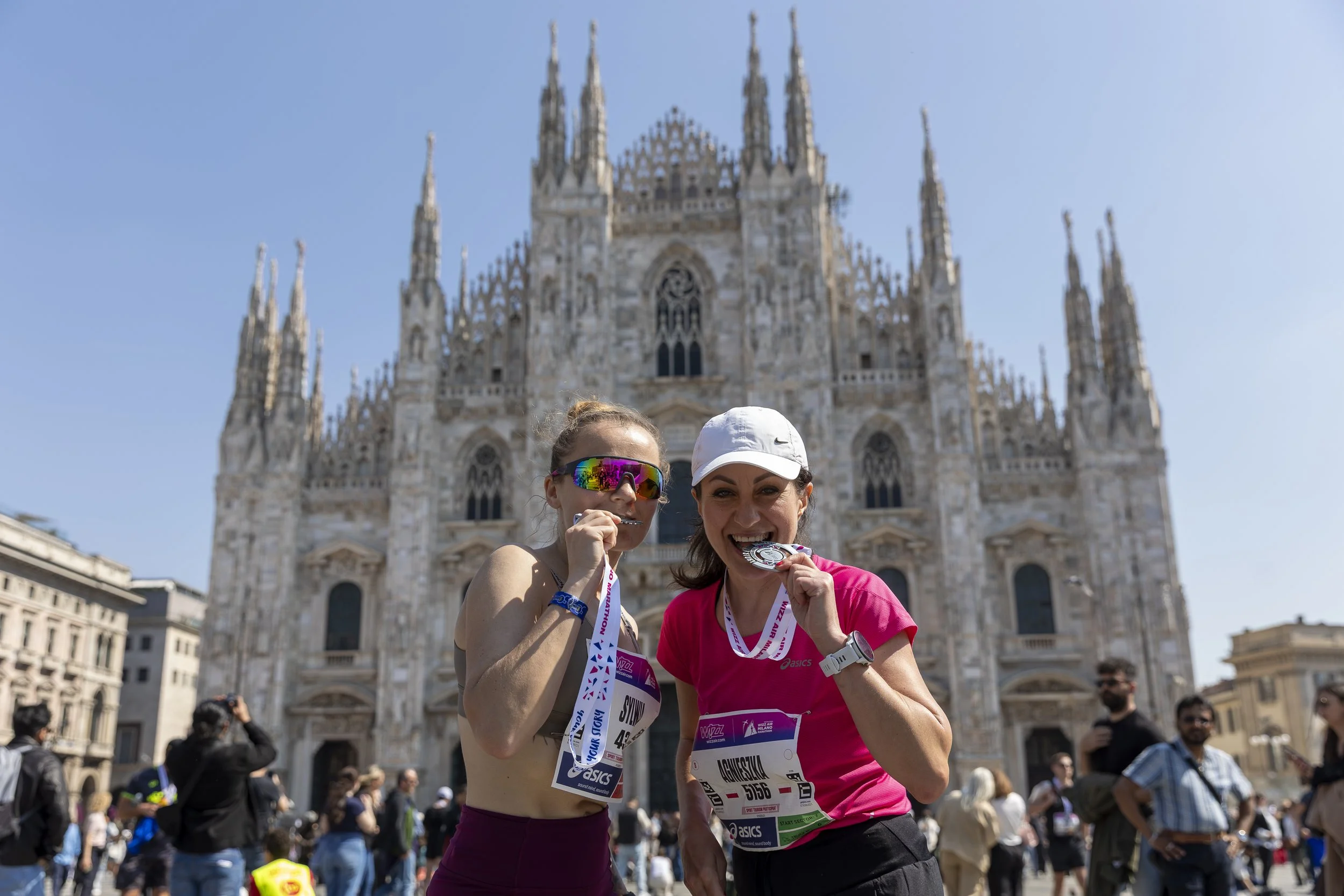 Two ladies biting their finishers' medals outside the famous Duomo di Milano cathedral.