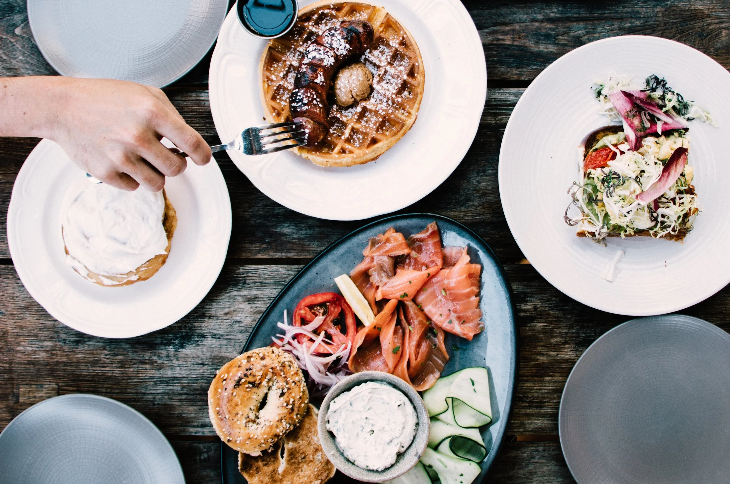 Brunch spread of waffle and salmon lox bagel on rustic table.
