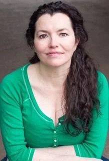 Caroline Colomei, headshot photo, wearing a green cardigan, posing indoors with a neutral background.