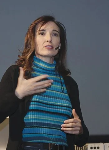 Tamara wearing a blue striped turtleneck sweater and black blazer, speaking at a lecture in University of Illinois.