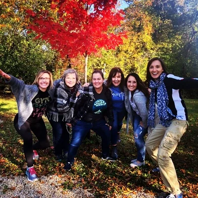 Tamara and other attendees at a talk smiling and taking a selfie outdoors during fall, with colorful autumn leaves in the background.