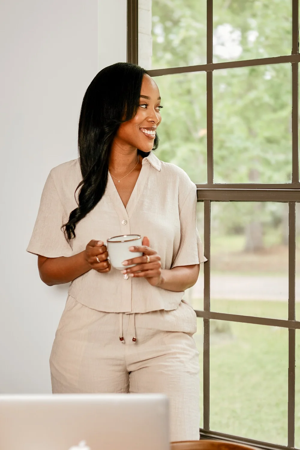 Megan Noel, founder of Noel + Willow, holding a coffee mug by a window