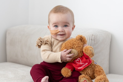 Toddler holding teddy bear with medical line into her nose.
