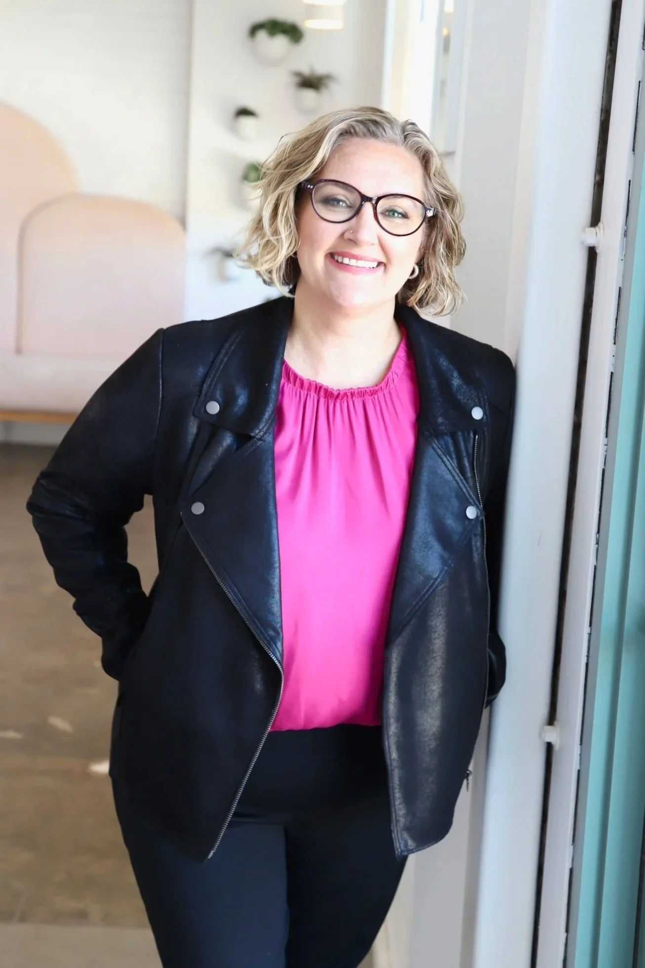 Jess Sato in a pink top and black leather jacket leaning against the wall