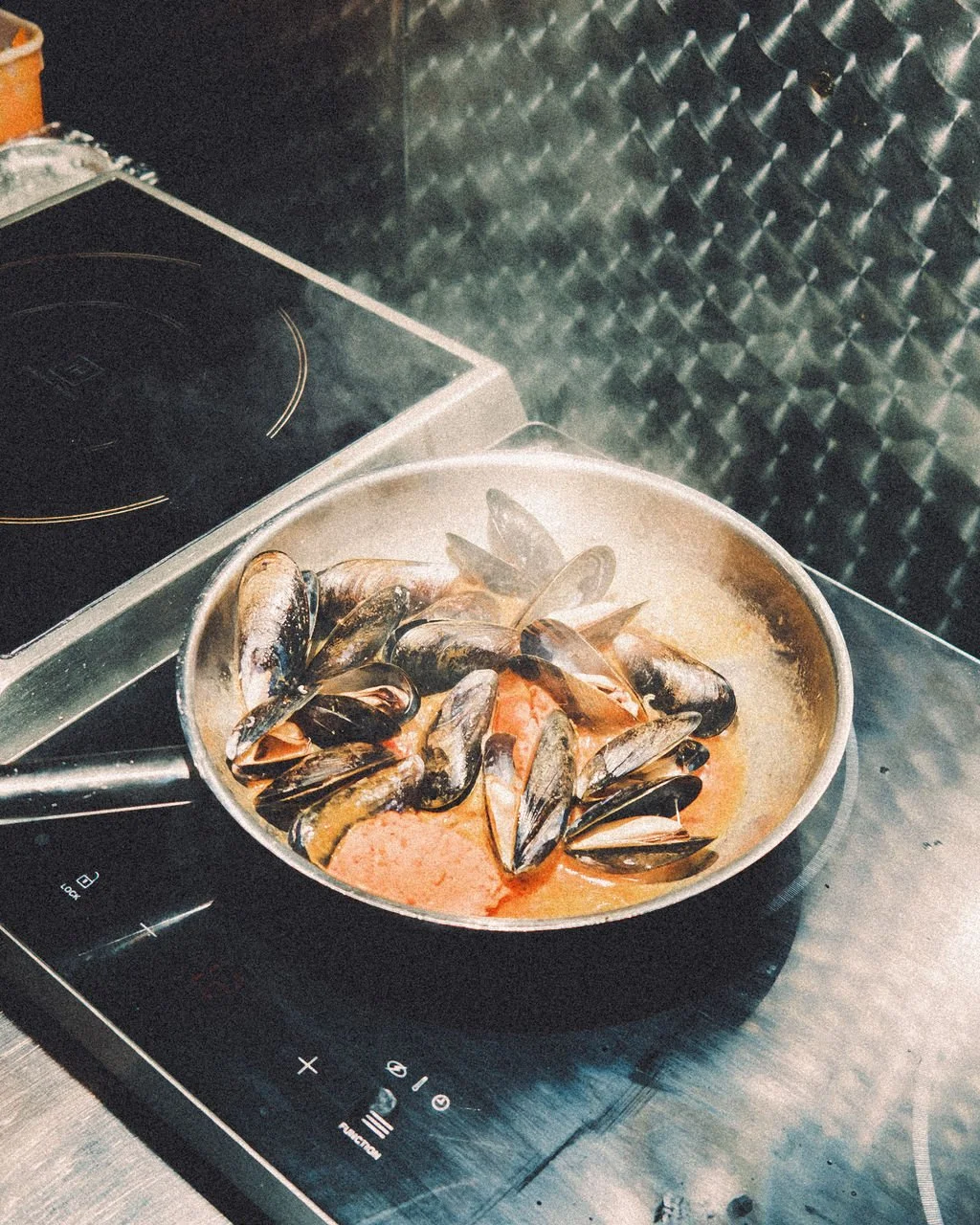 Cooking mussels in a pan on the stove with a tomato-based sauce.