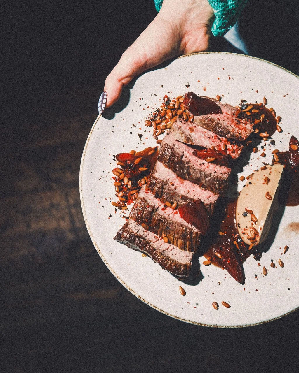 Sliced cooked steak topped with seasoning and sunflower seeds on a white plate