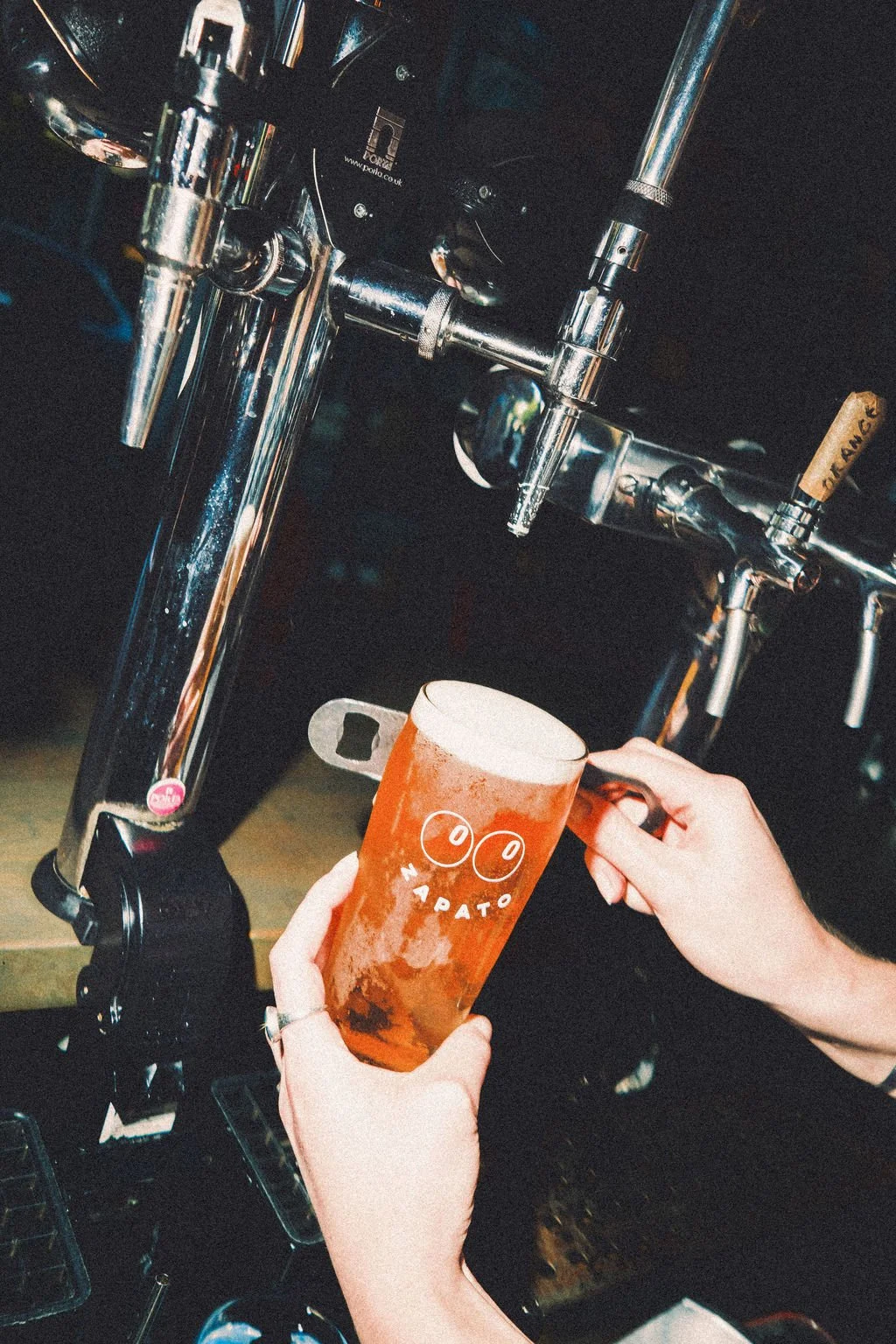 Person filling a glass with draft beer from a tap at a bar or brewery.