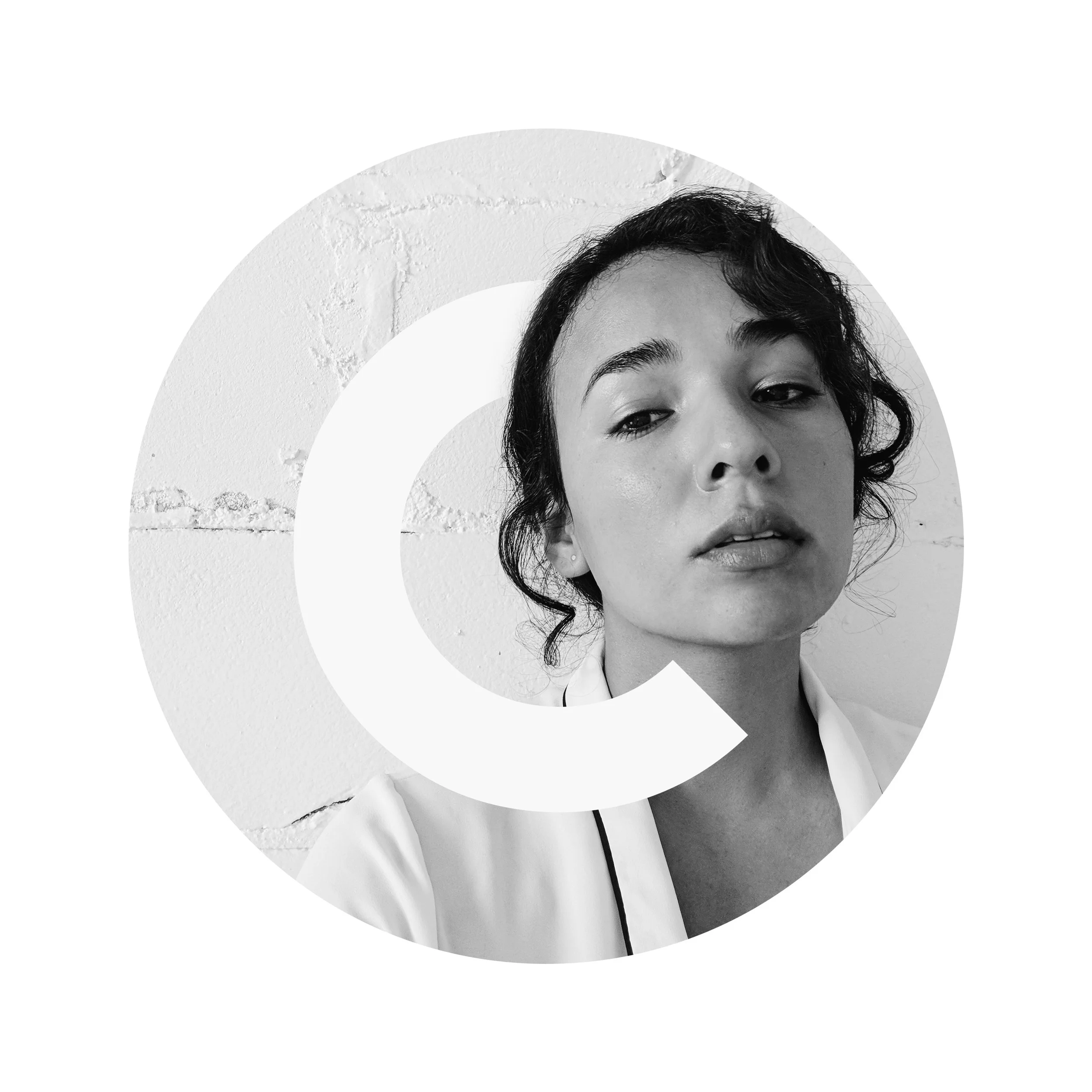 Black and white portrait of a woman with wavy hair, looking slightly downward, against a plain wall background.