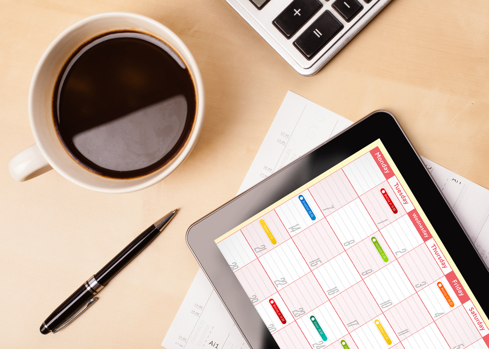 Workplace with tablet pc showing calendar and a cup of coffee on a wooden work table close-up.jpeg