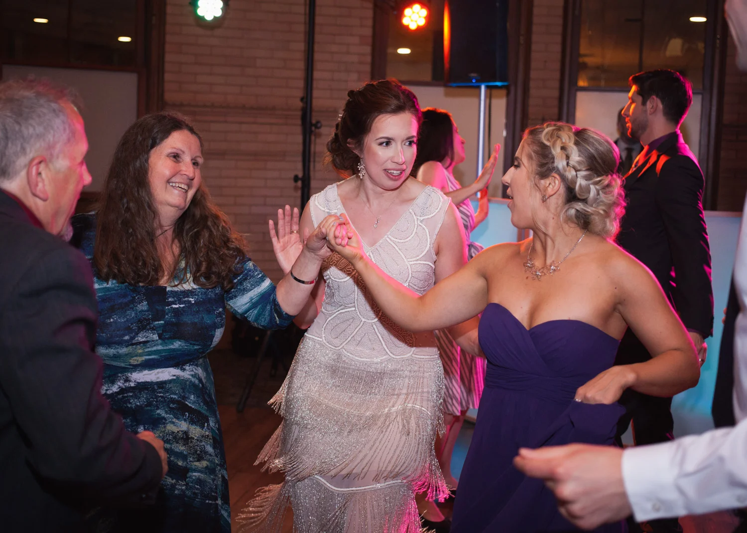 Bride in white fringe flapper dress dances with wedding guests.