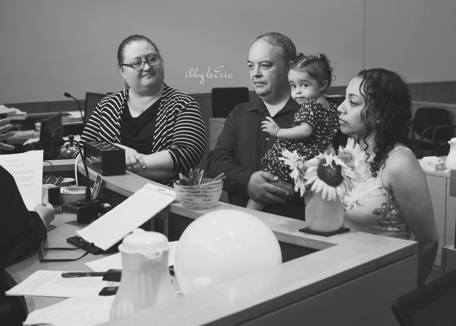 Black and white photo of girl peeking at the camera during her family's adoption in Greenfield courtroom.