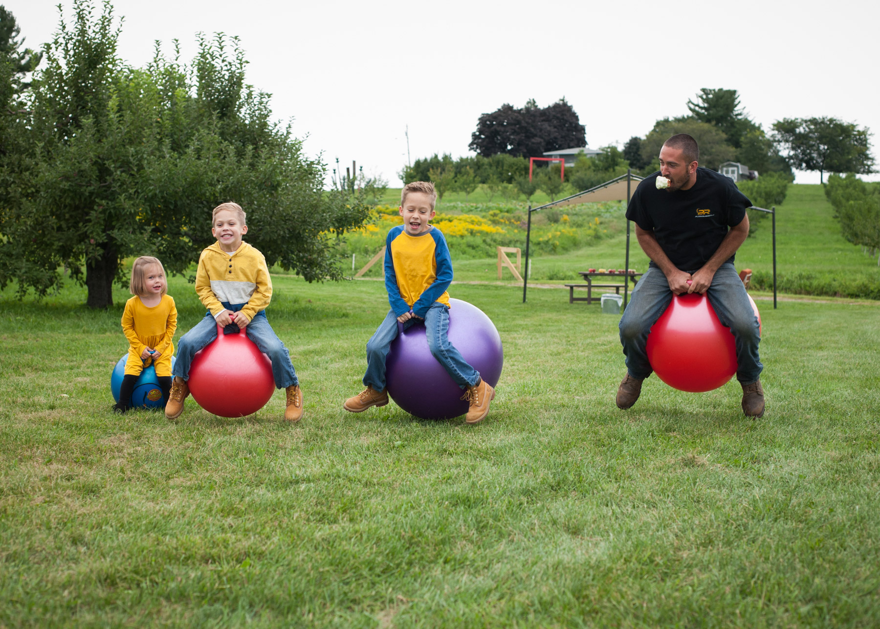 Three kids and their dad line up and race on giant bouncing balls in a field.