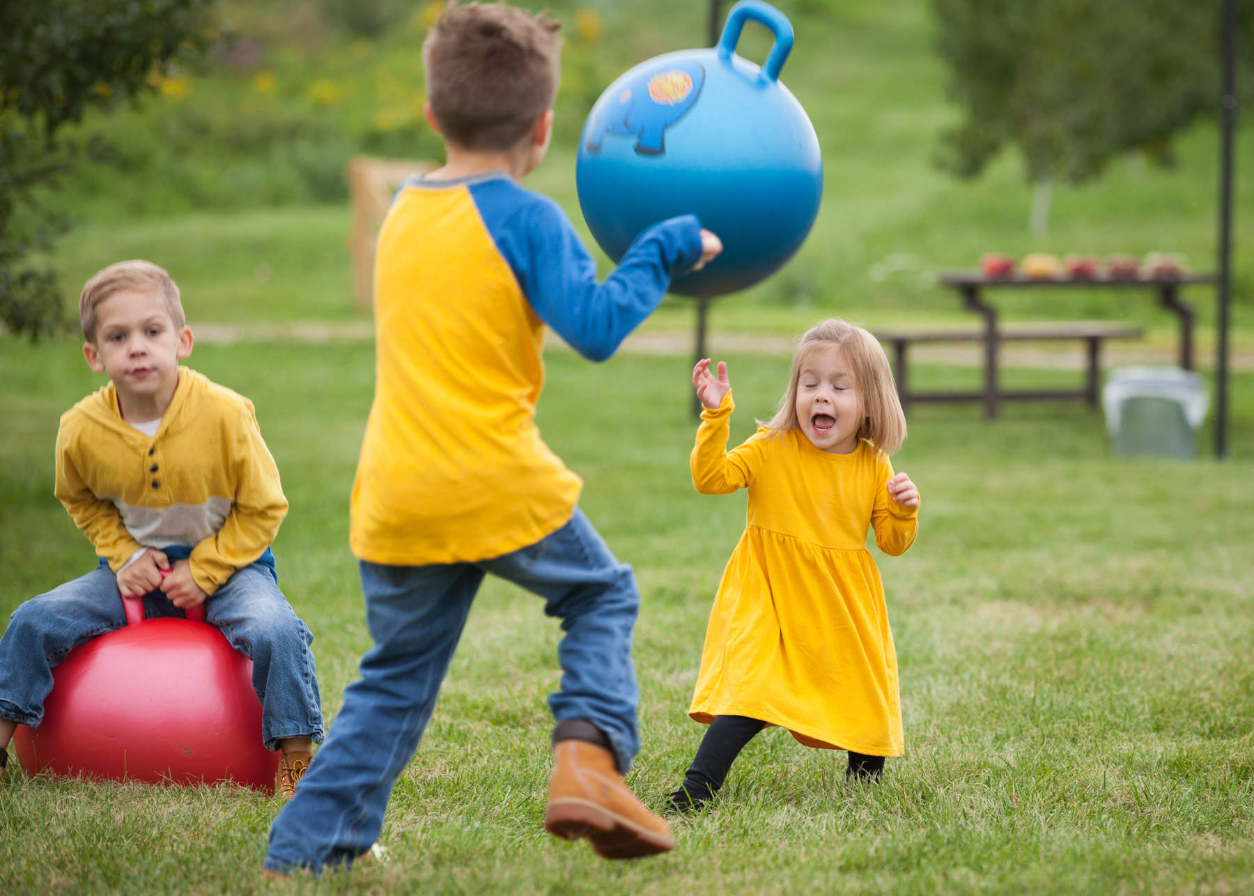 Toddler girl in yellow dress makes a shocked face as she dodges the ball her is throwing at her.