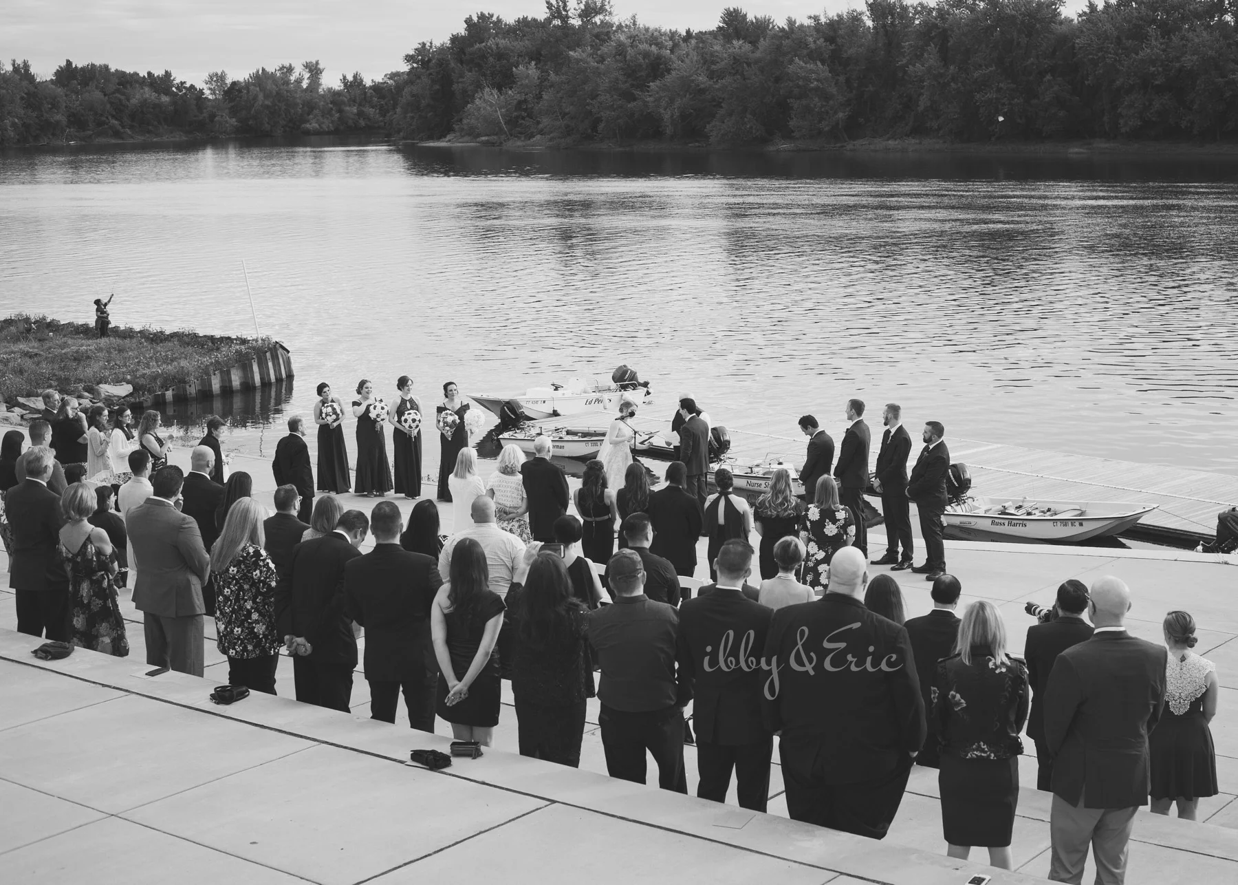 Black and white wide angle photo showing a riverfront wedding ceremony at the Glastonbury Boathouse in Connecticut.