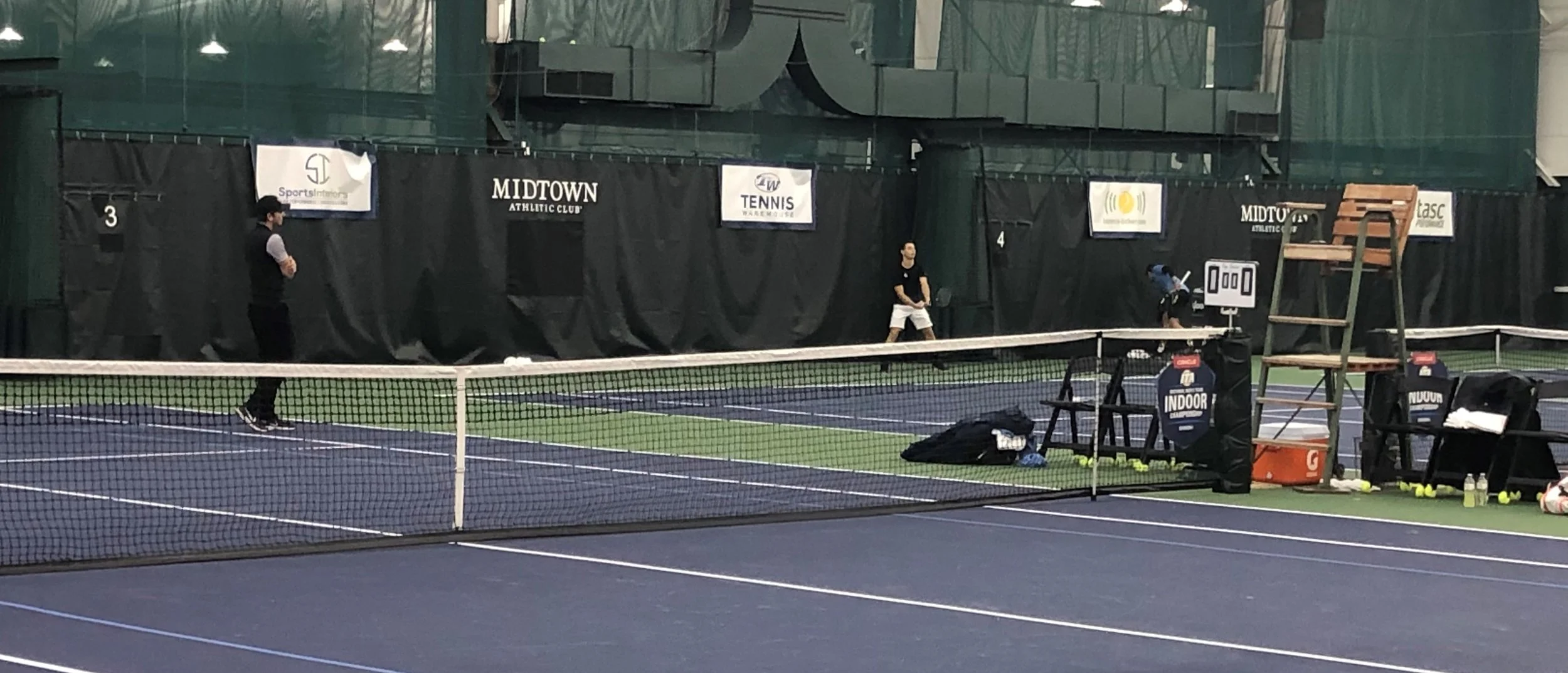 Action at the ITA National Men’s Team Indoor Championship with Sports Interiors banner