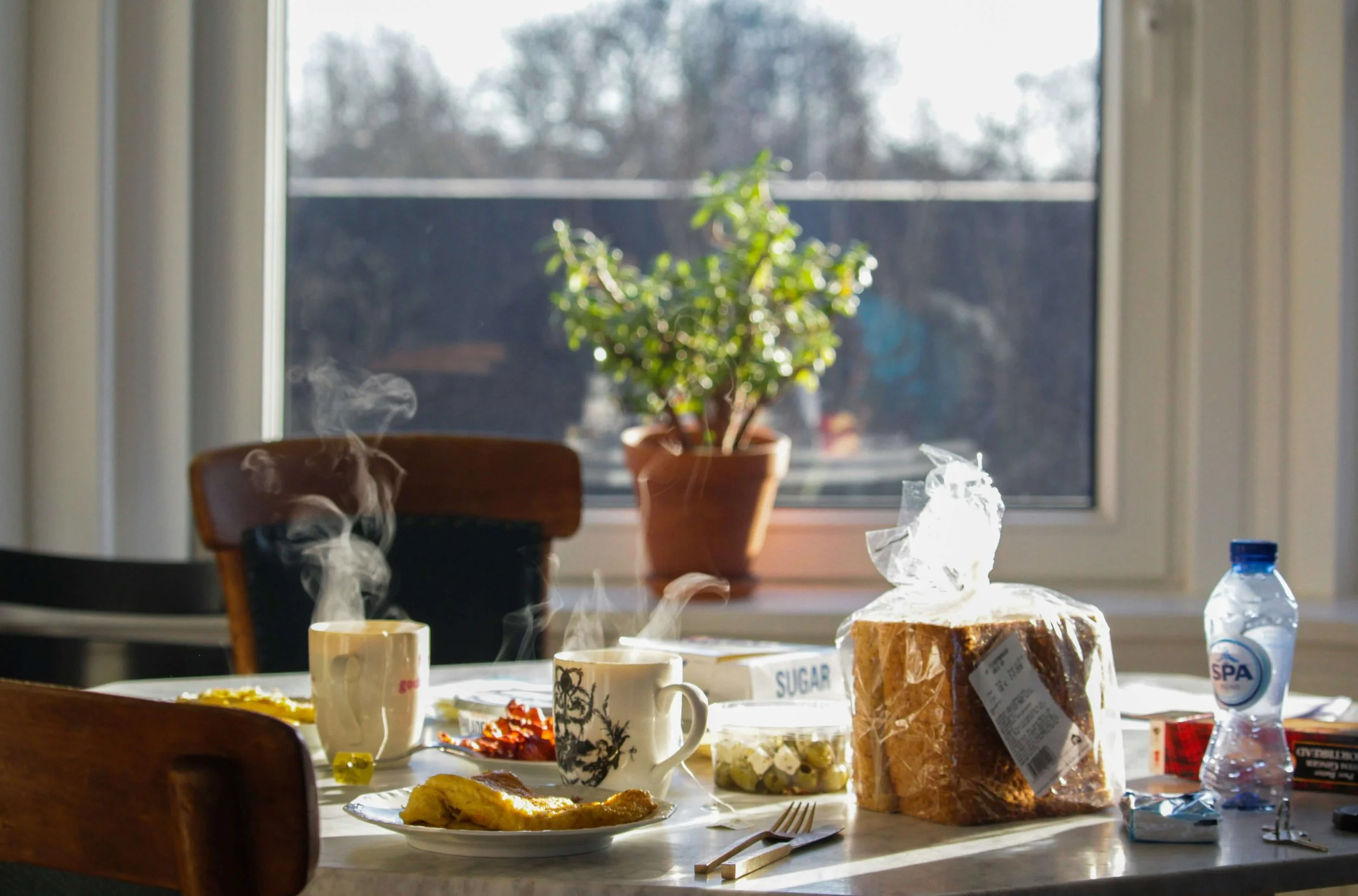 Breakfast table with bread, coffee, and a warm meal in natural morning light