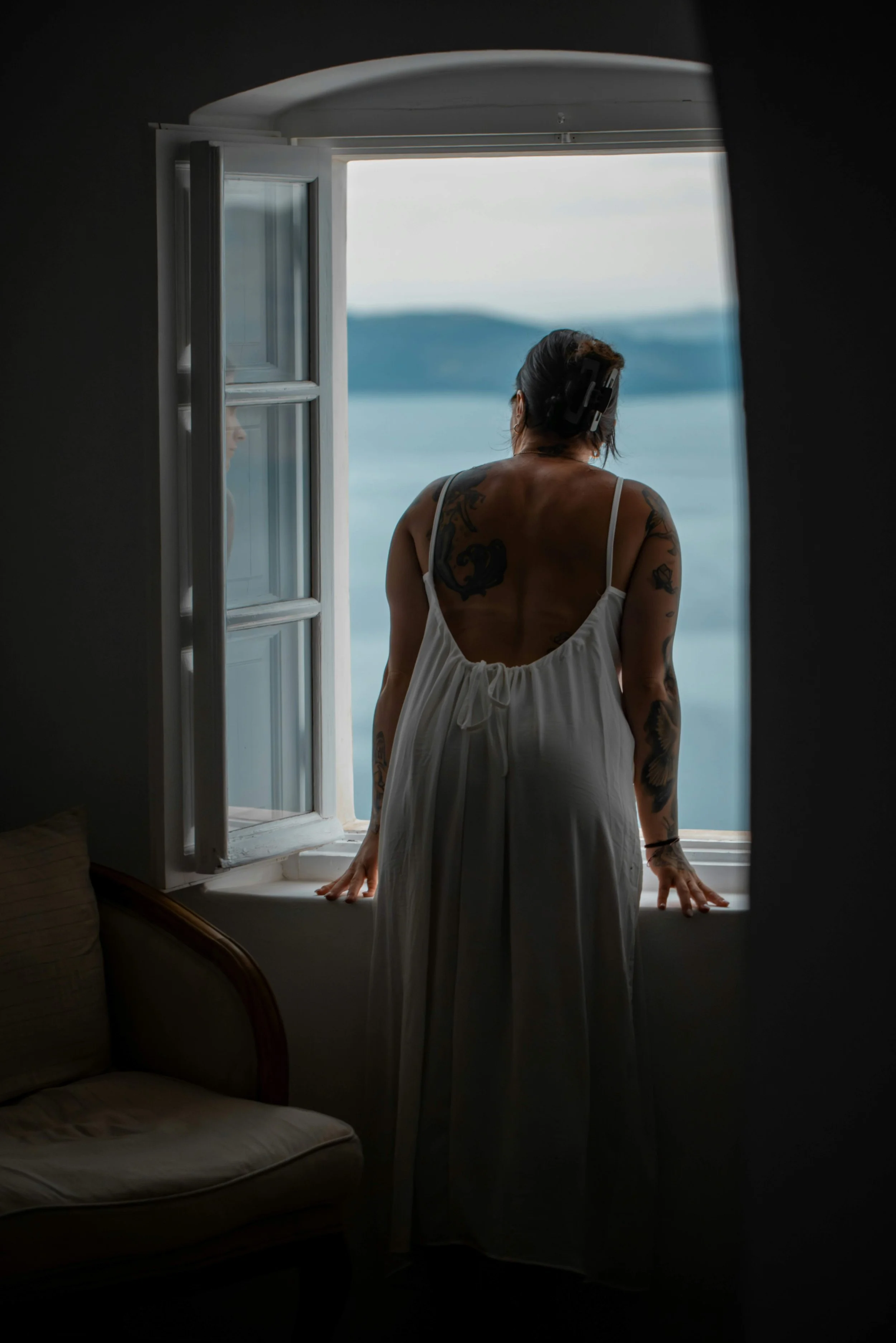 Woman standing by a window looking outside in natural light.