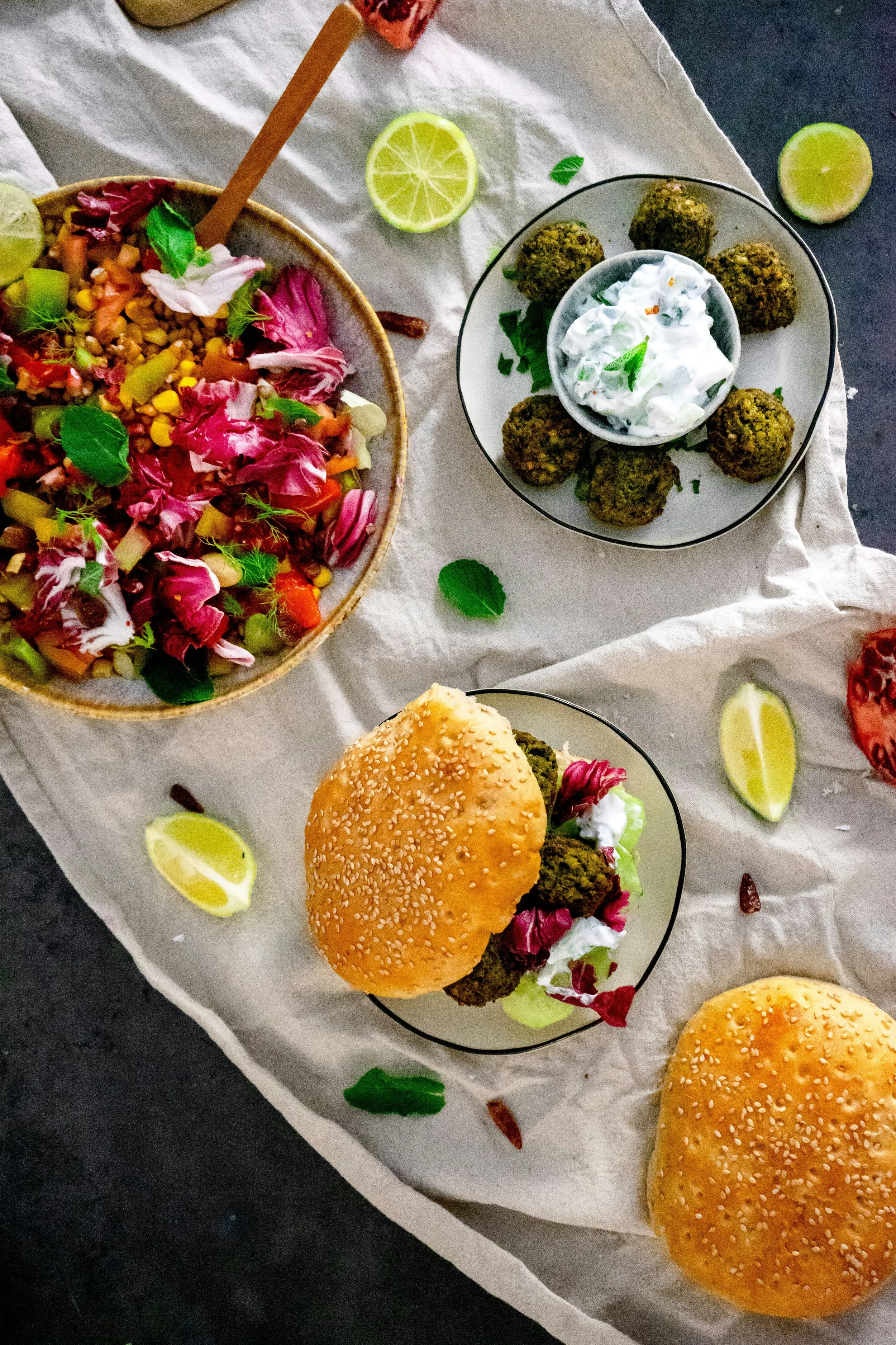 Colorful Mediterranean-inspired meal with falafel, fresh salad, yogurt sauce, and sandwiches on a table.