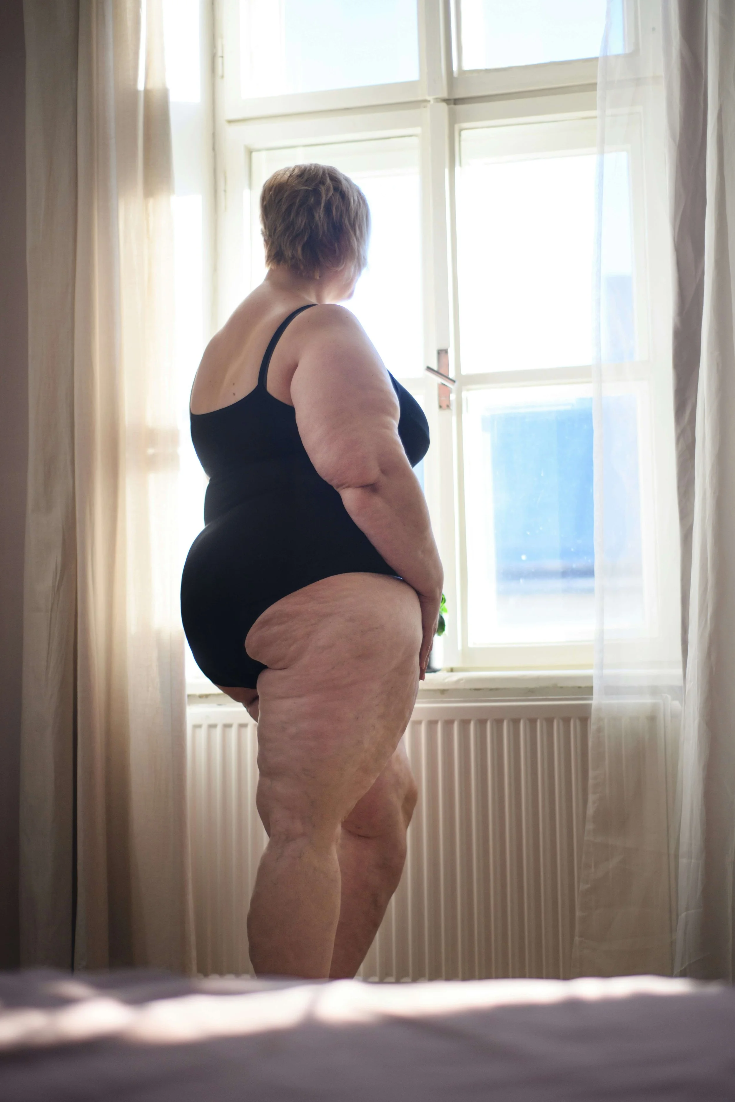 Person in a black bodysuit standing by a window