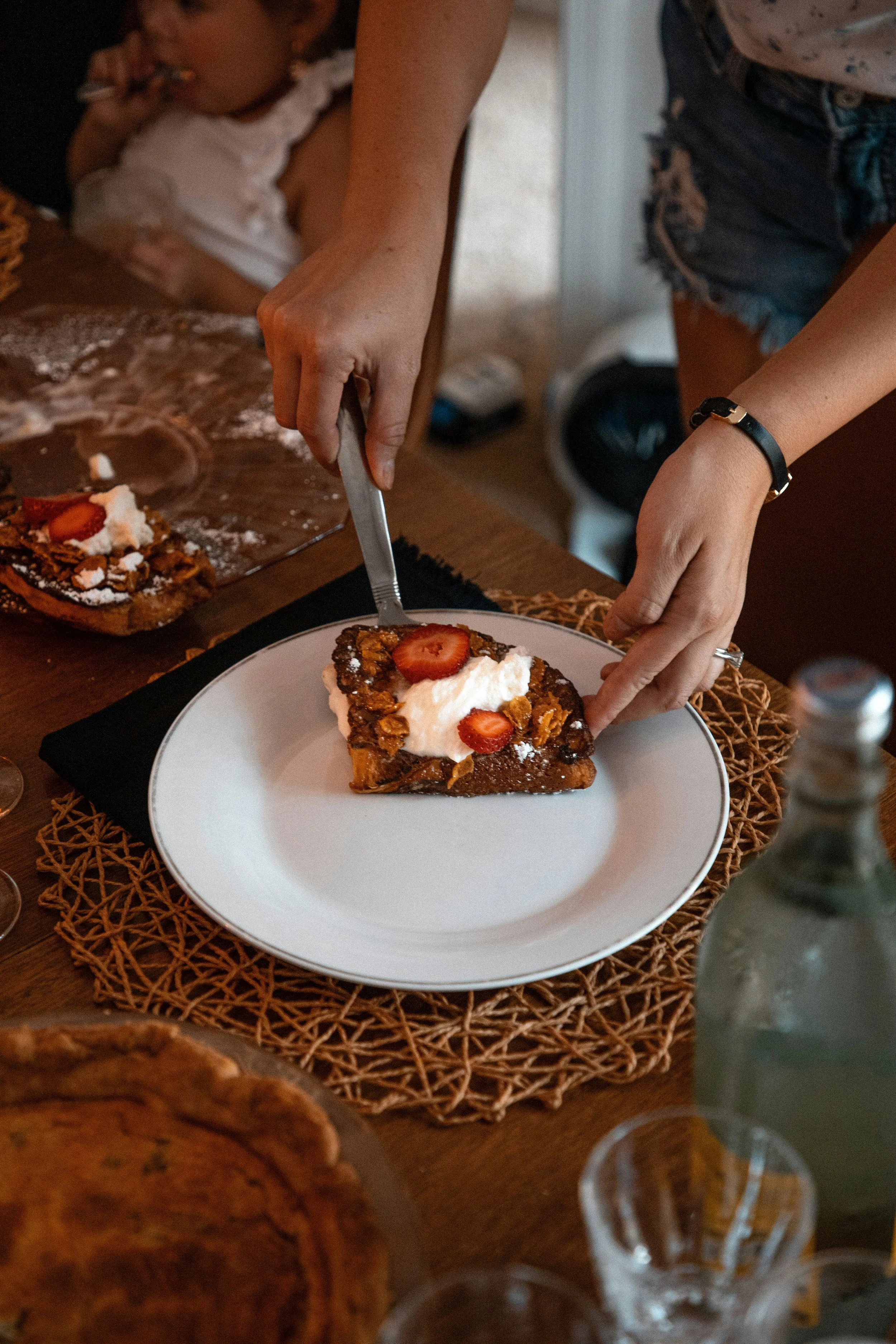 Person serving a slice of cake onto a plate during a shared meal.