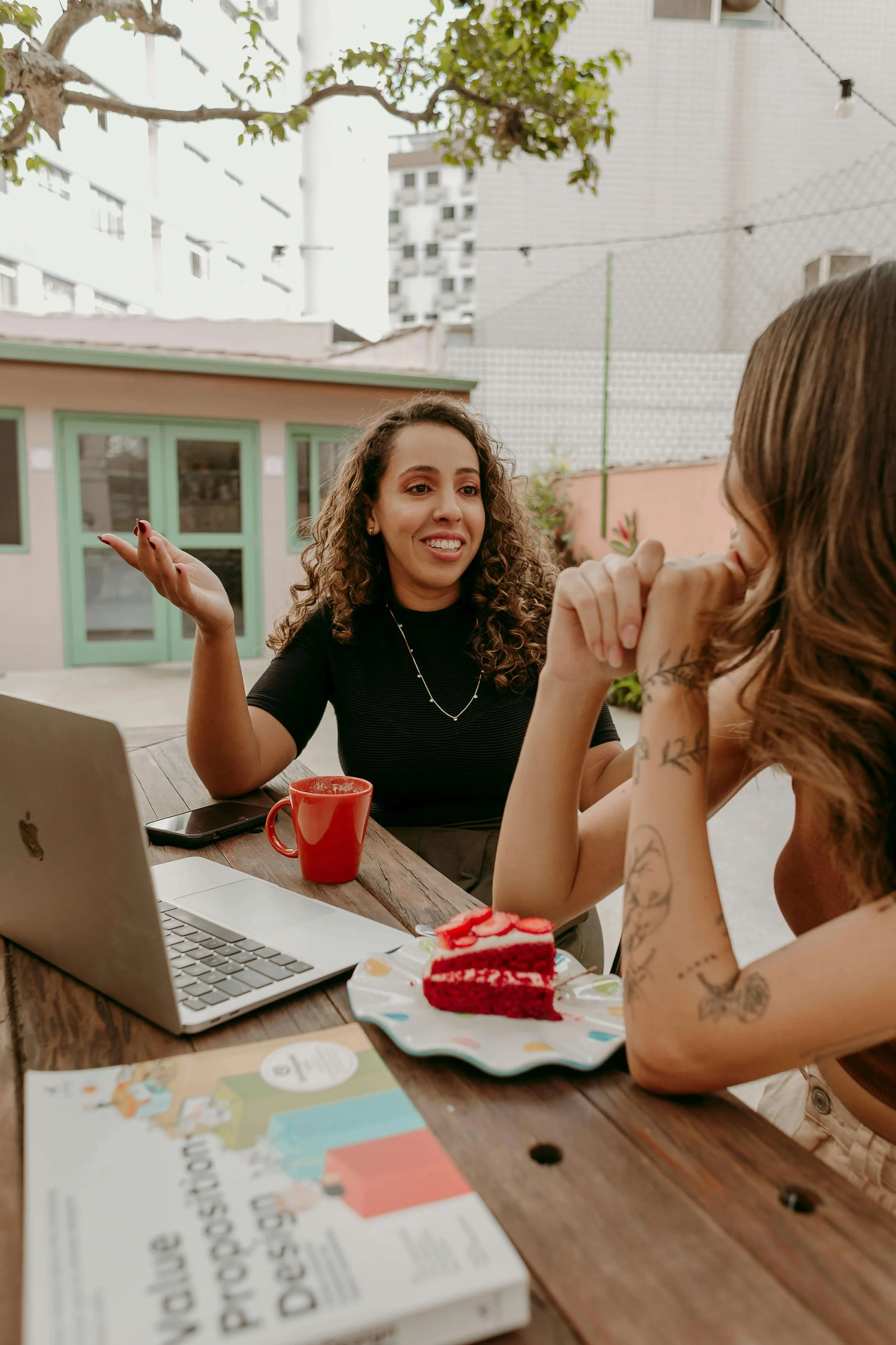Two women talking over coffee and dessert while sitting together at an outdoor table.