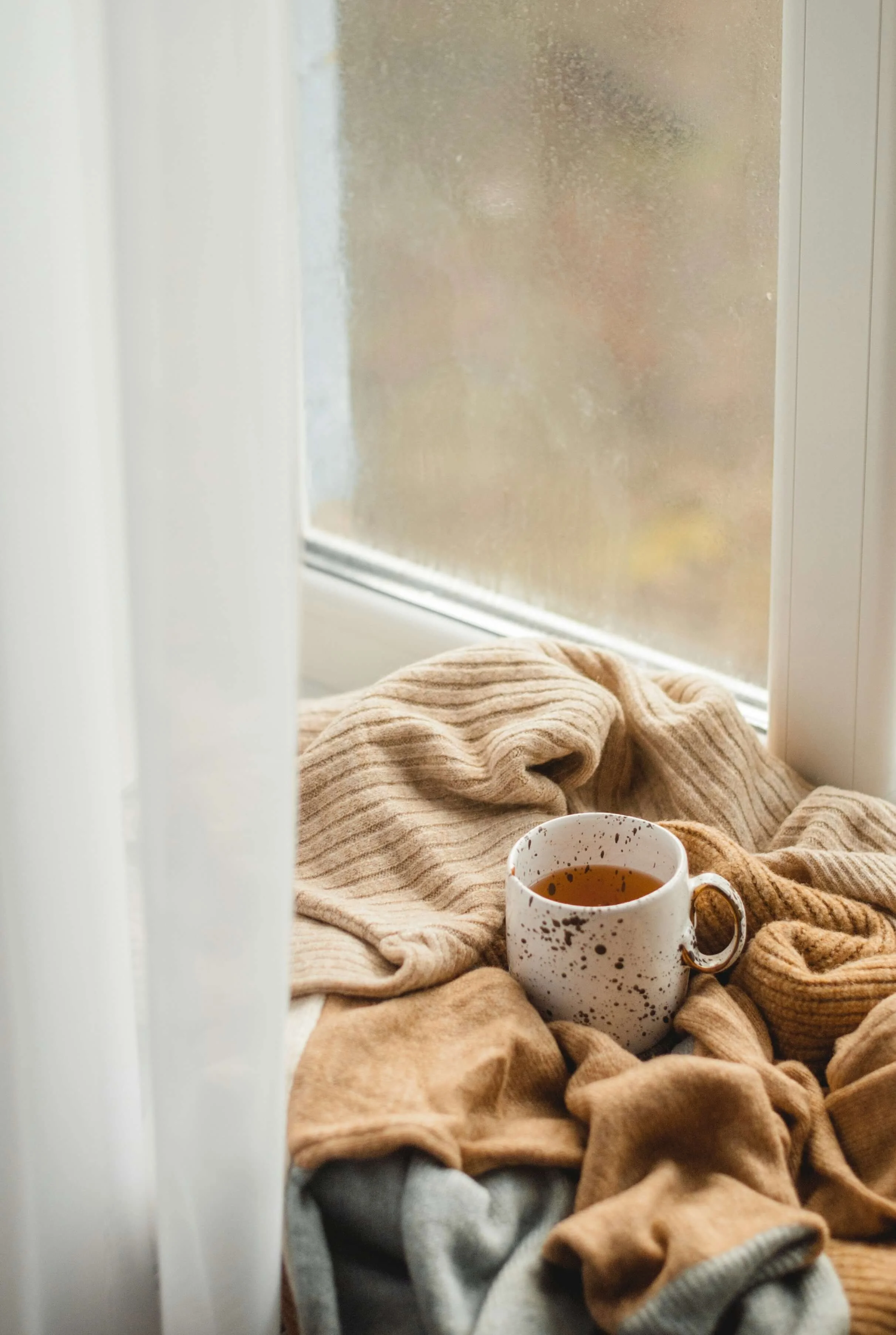 Cup of tea resting on a blanket beside a window